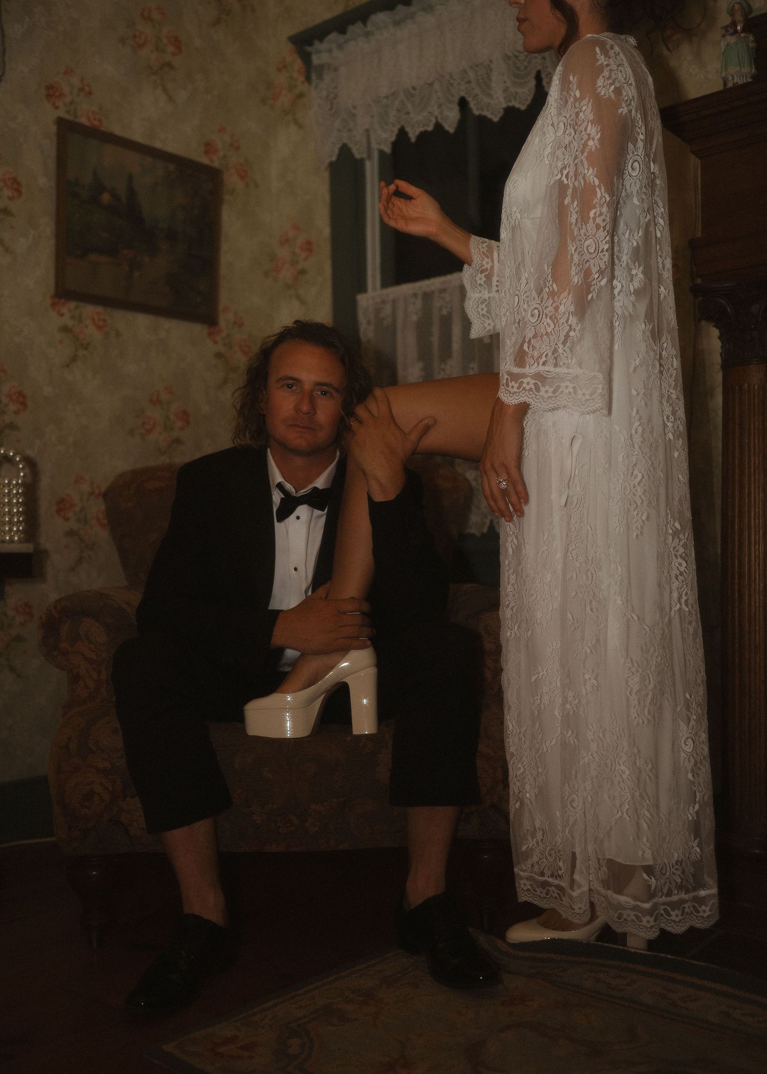 Vintage-style interior scene with white lace dresses and formal attire in a dimly lit room.