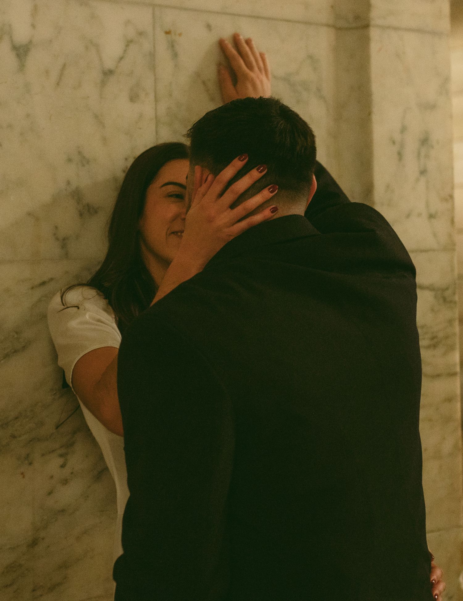 A tender embrace captured in warm tones against a textured marble wall.