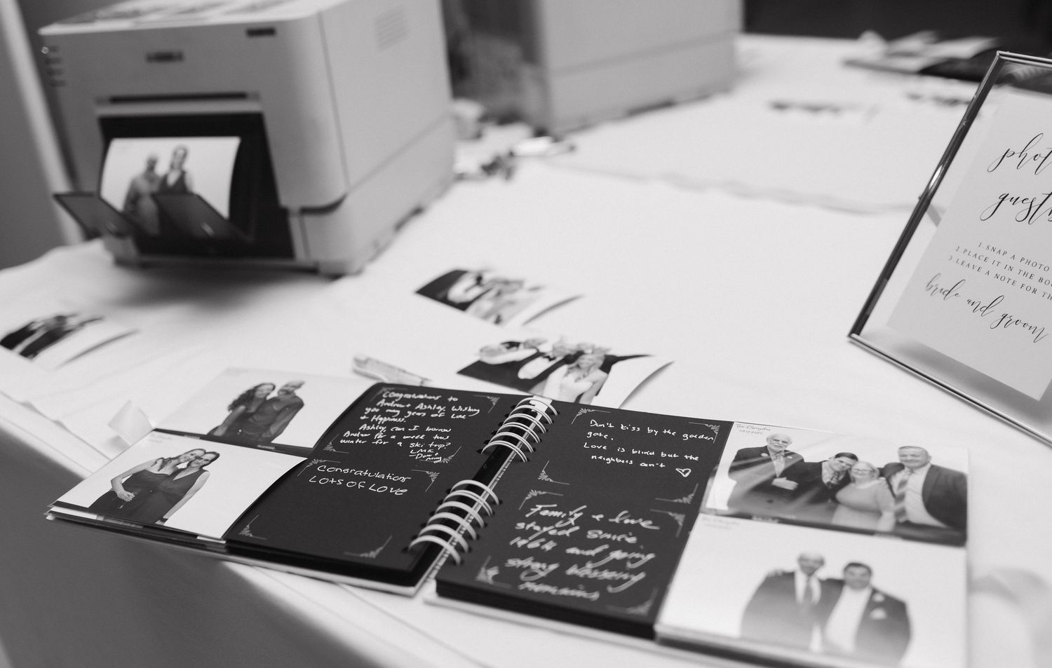 Wedding guest book with black pages and polaroid photos laid out on white table.