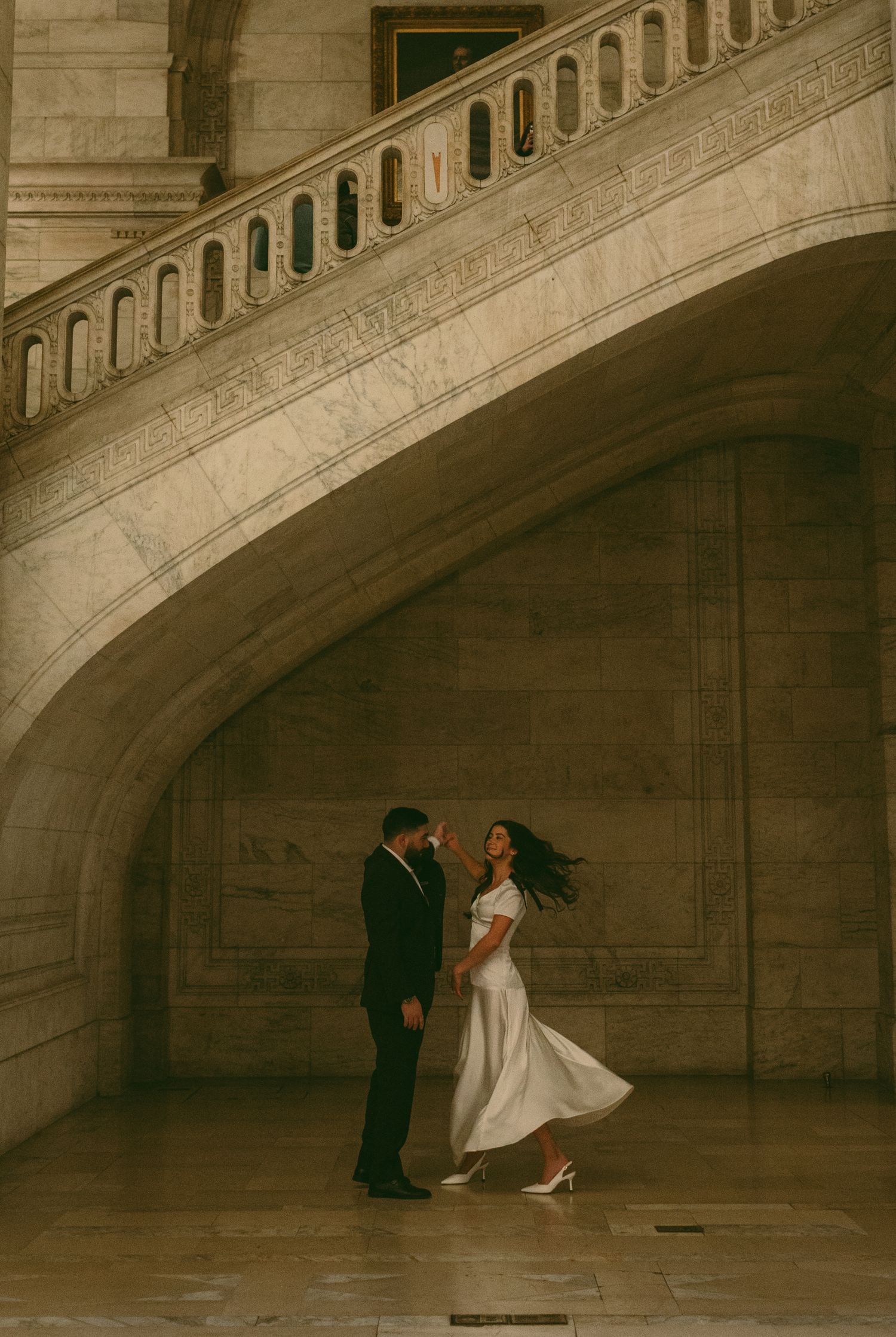 A couple in formal wear dances beneath a grand marble archway in an elegant building.