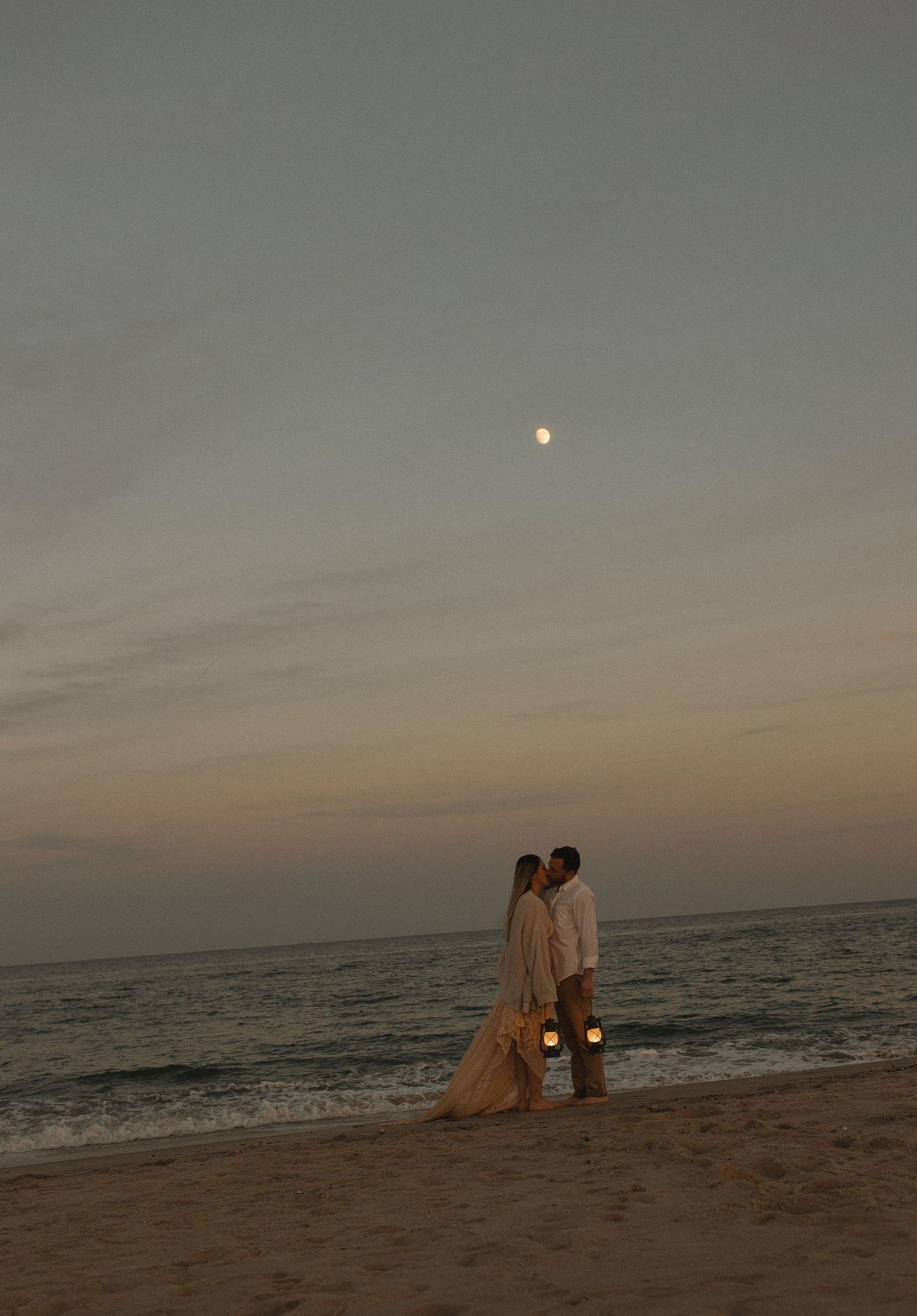 Romantic sunset beach scene with silhouettes walking along the shoreline at dusk.