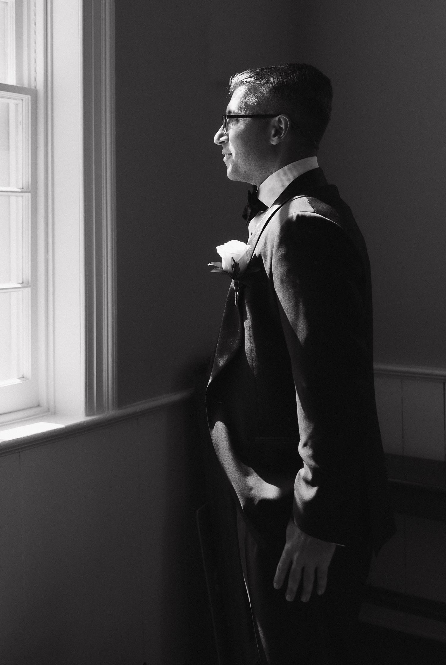 Dramatic window lighting illuminates figures in formal attire in a minimalist room.