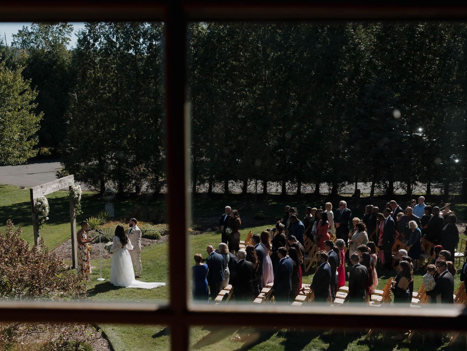 Outdoor wedding ceremony with guests seated in rows among tall trees.