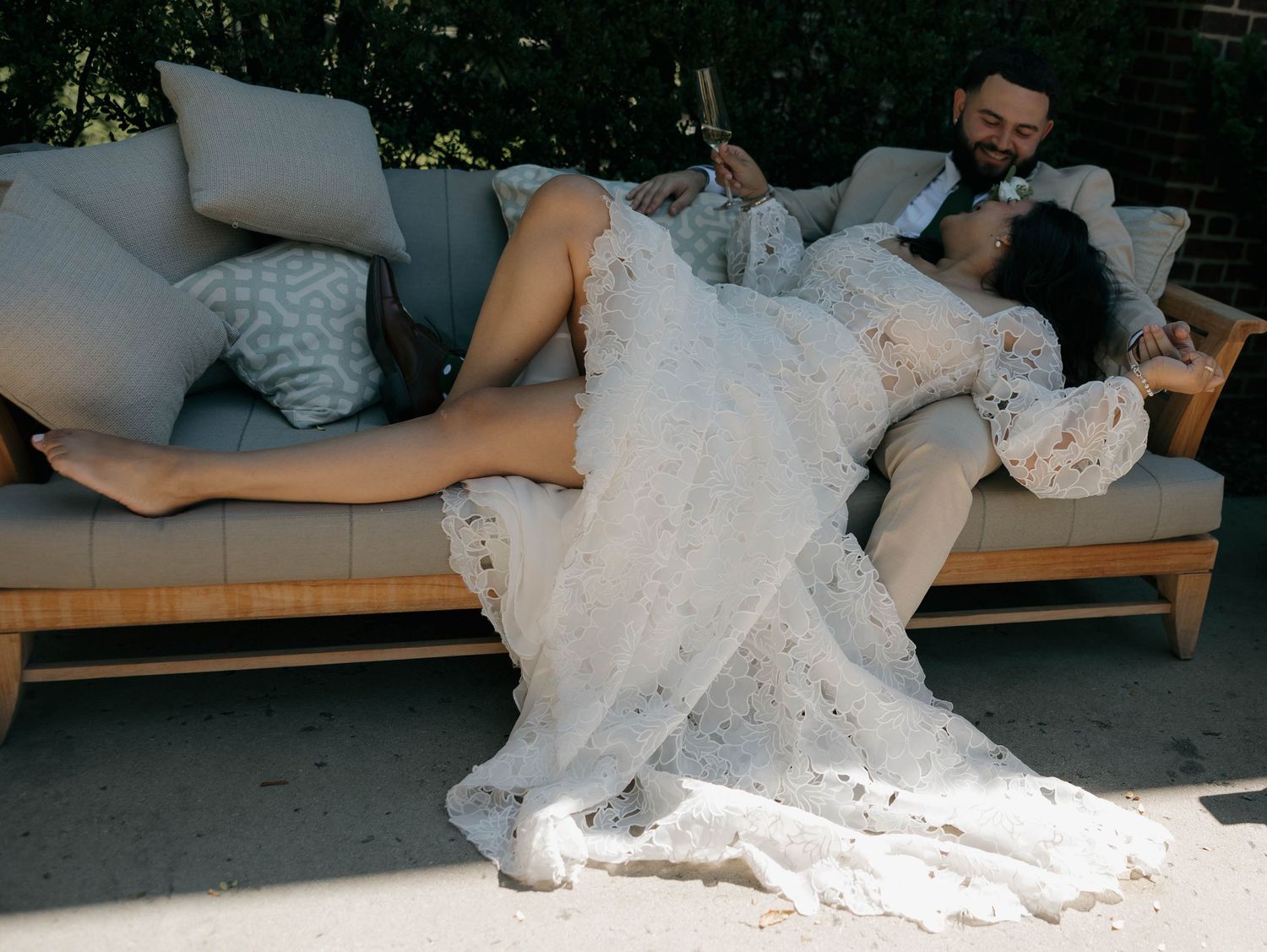 Newlyweds resting on outdoor patio furniture with white wedding dress flowing.