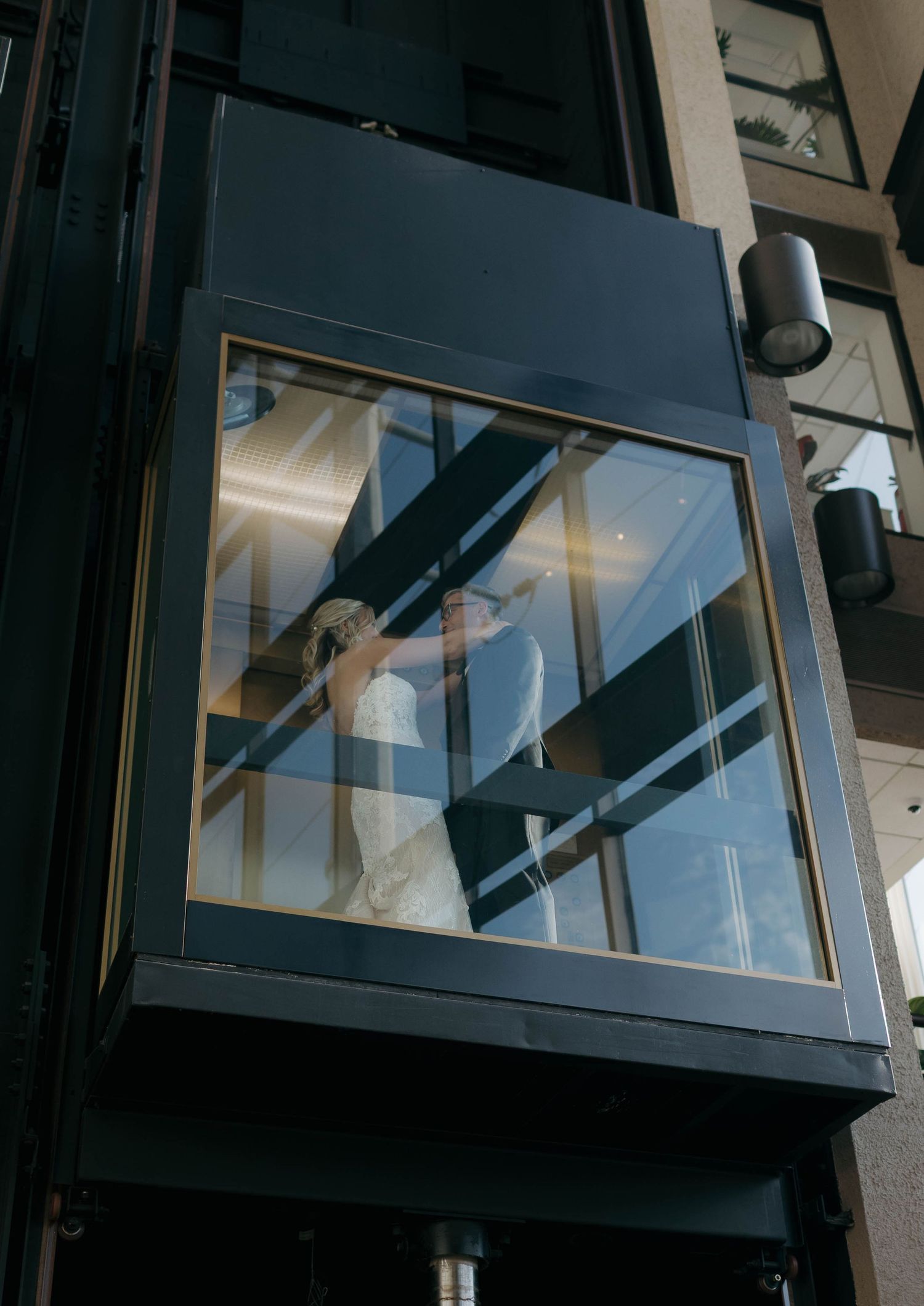 Modern glass elevator shaft with architectural details and lighting mounted on exterior wall.