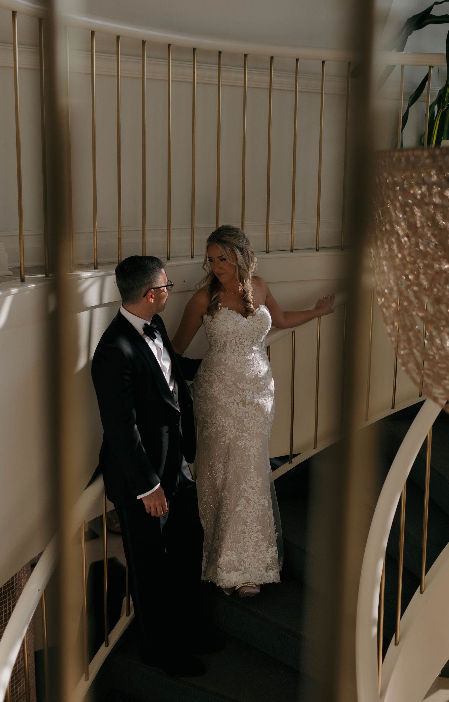 A wedding couple shares a tender moment on a curved staircase with dramatic lighting.