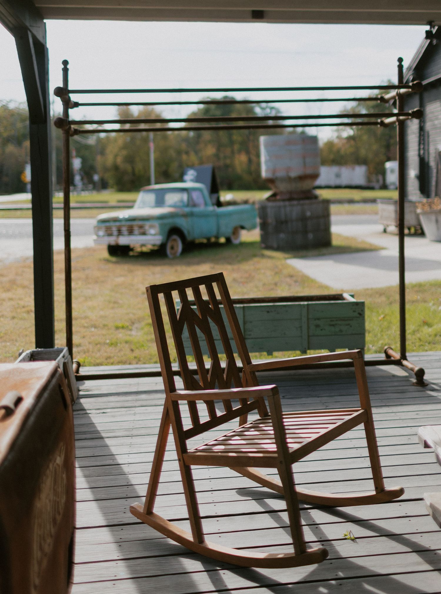Wooden rocking chairs cast shadows on a sunlit porch in a rustic outdoor setting.