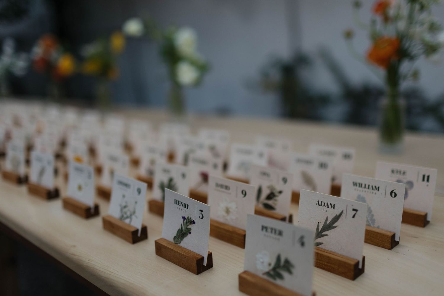 Wedding place cards arranged in neat rows with wooden holders on a light-colored table.