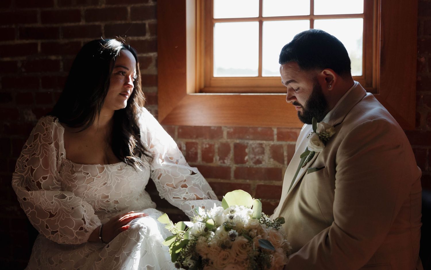 Romantic wedding scene with sunlight streaming through windows in a historic brick venue.