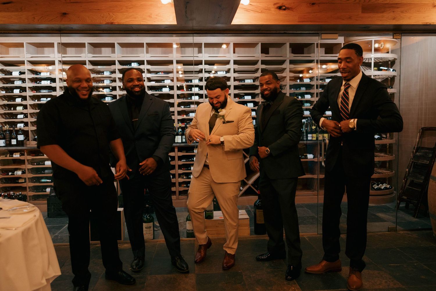 Wedding party poses together against wine rack backdrop in formal attire.