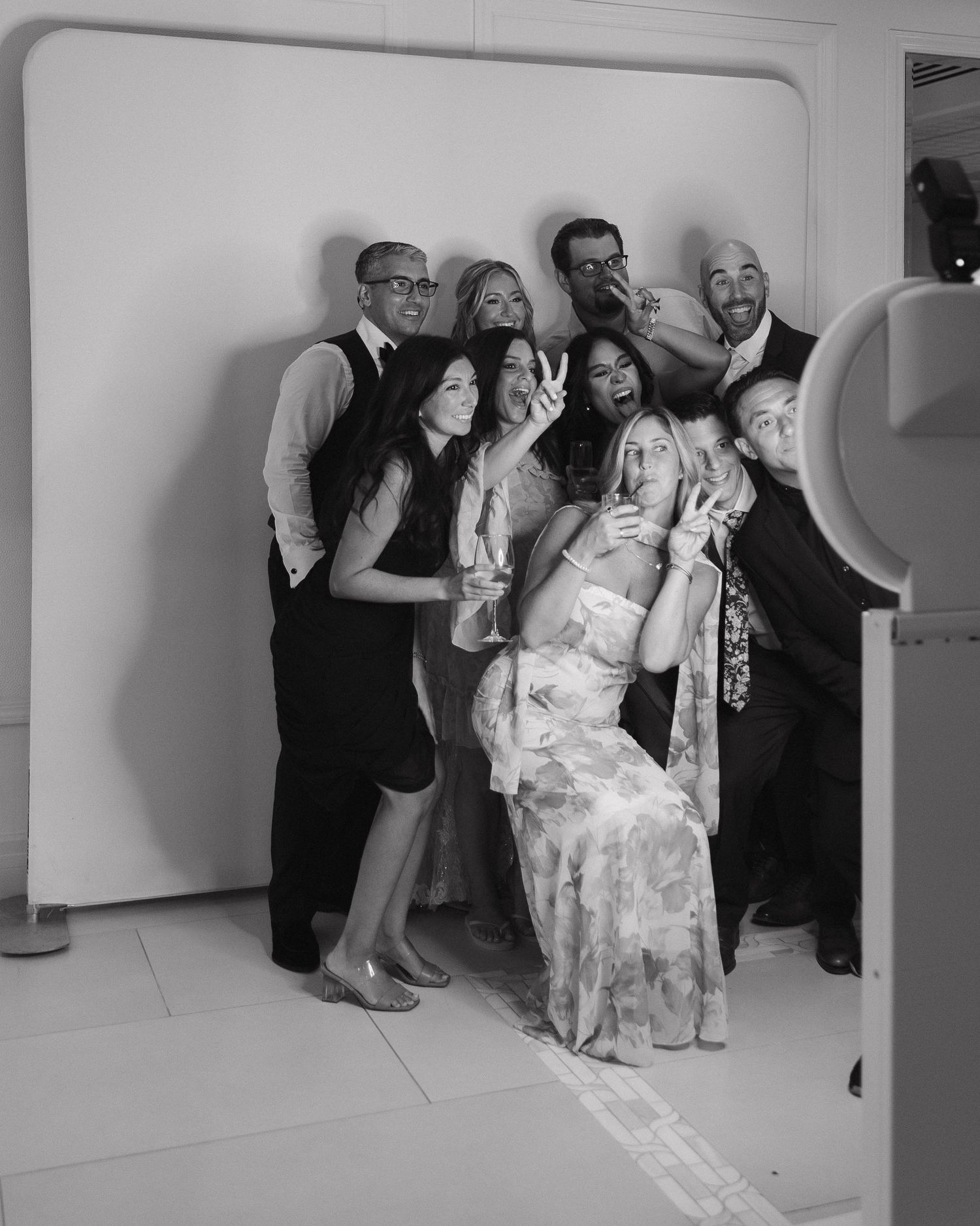Wedding party poses for creative group photos against a white wall.