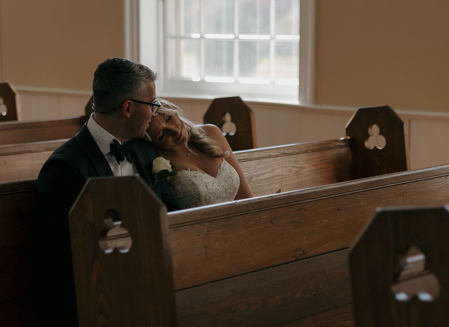 Intimate moment between newlyweds in wooden church pews during wedding ceremony.