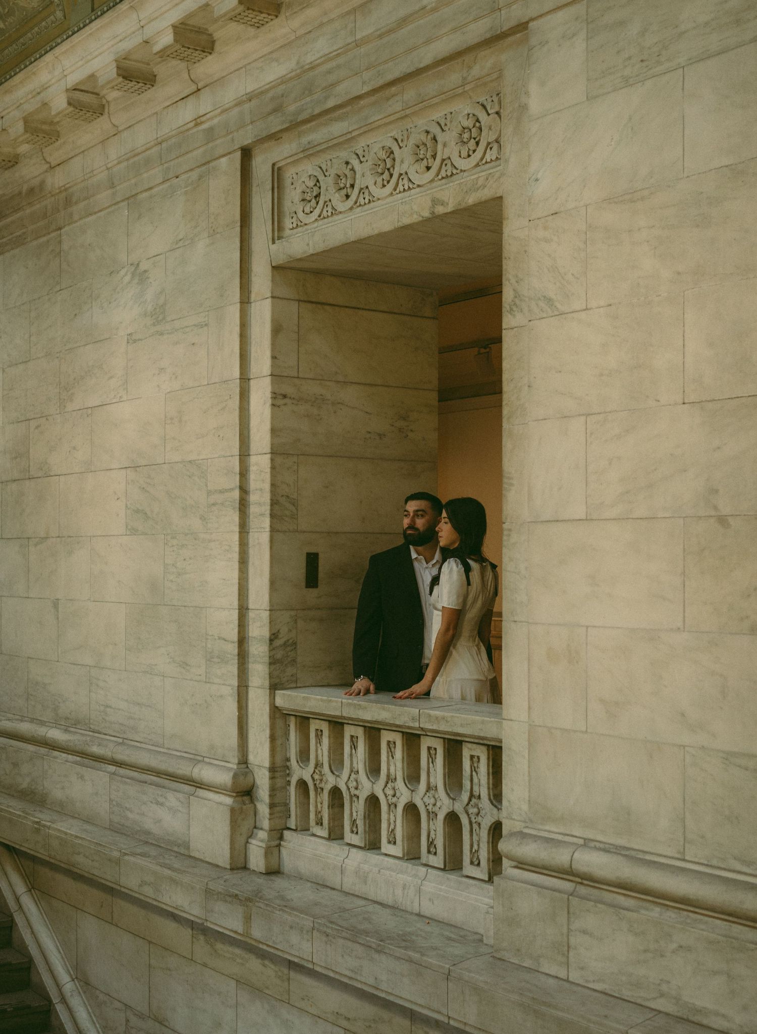 A couple stands together in an elegant marble hallway with ornate architectural details.