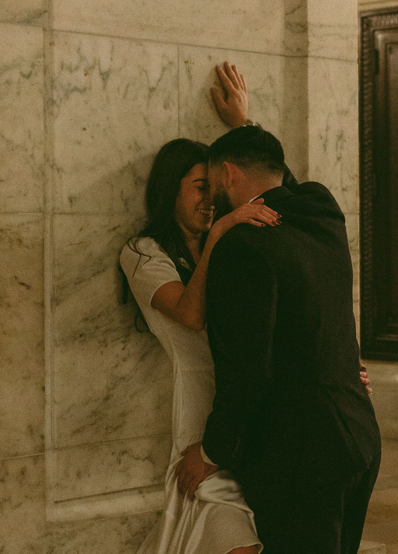 An intimate moment between a couple against a marble wall in moody lighting.