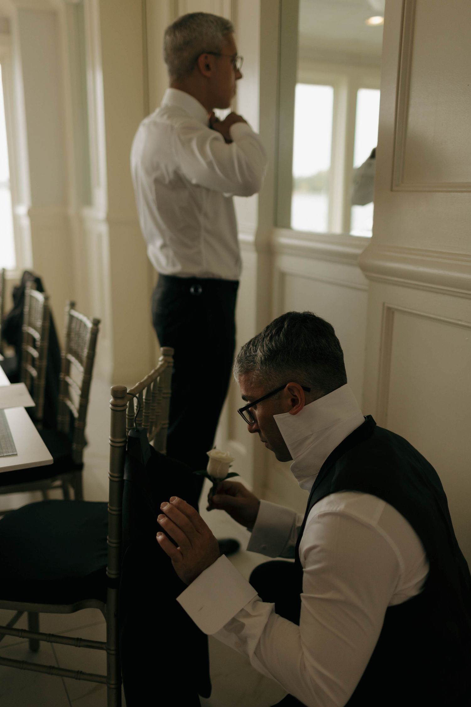 Two people in formal attire adjusting their outfits in an elegant hallway.