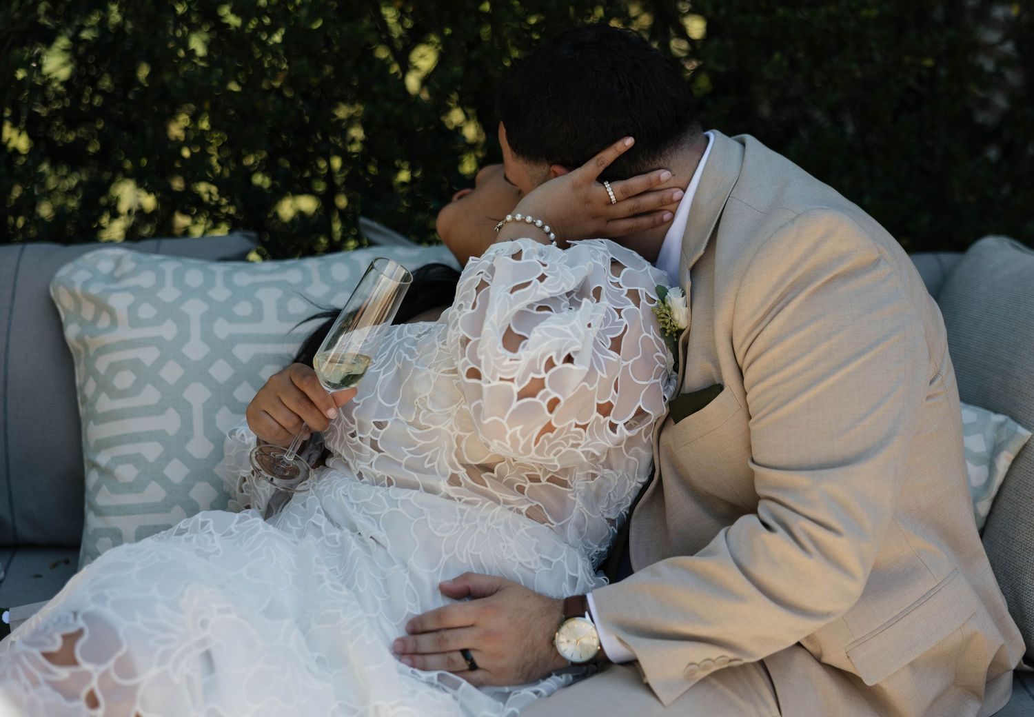 An intimate wedding moment captured outdoors with the couple reclining on grey patio furniture.