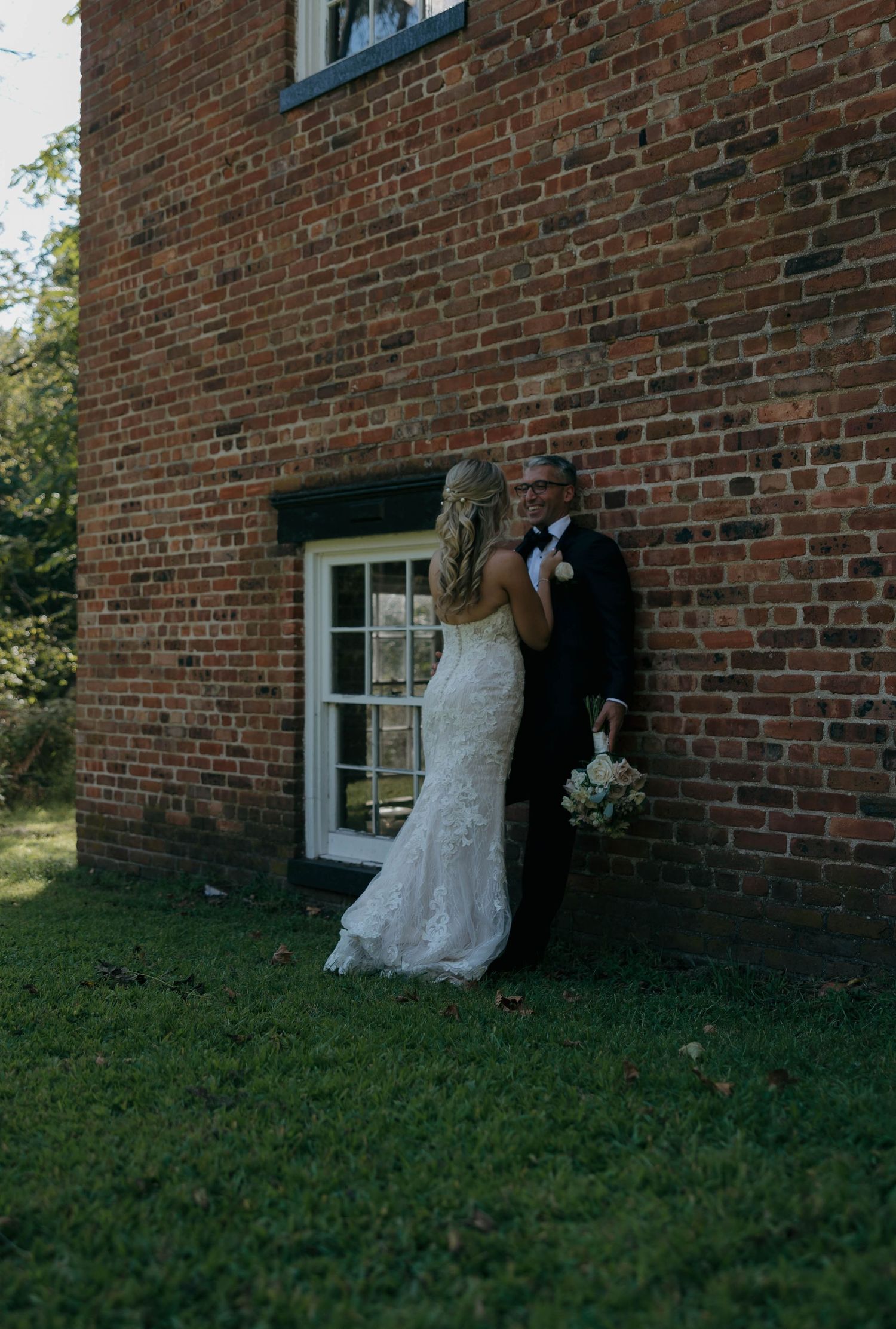 A wedding couple poses intimately against a historic brick building with white window frames.