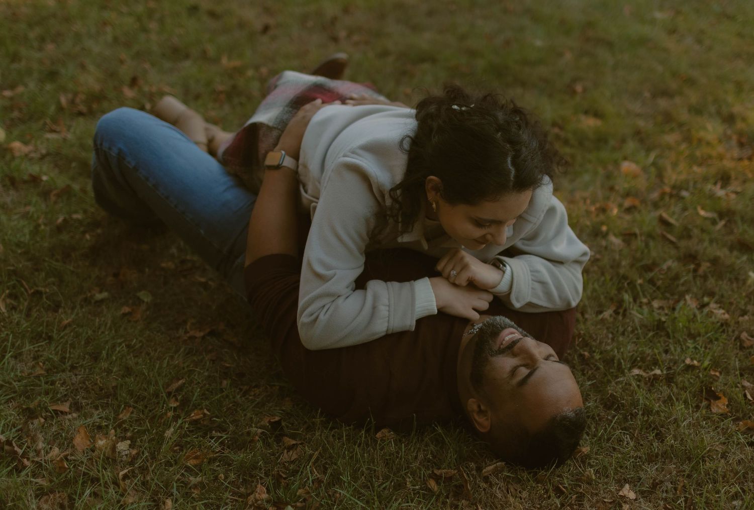 Couple lying on grass in casual attire during a relaxed outdoor moment.