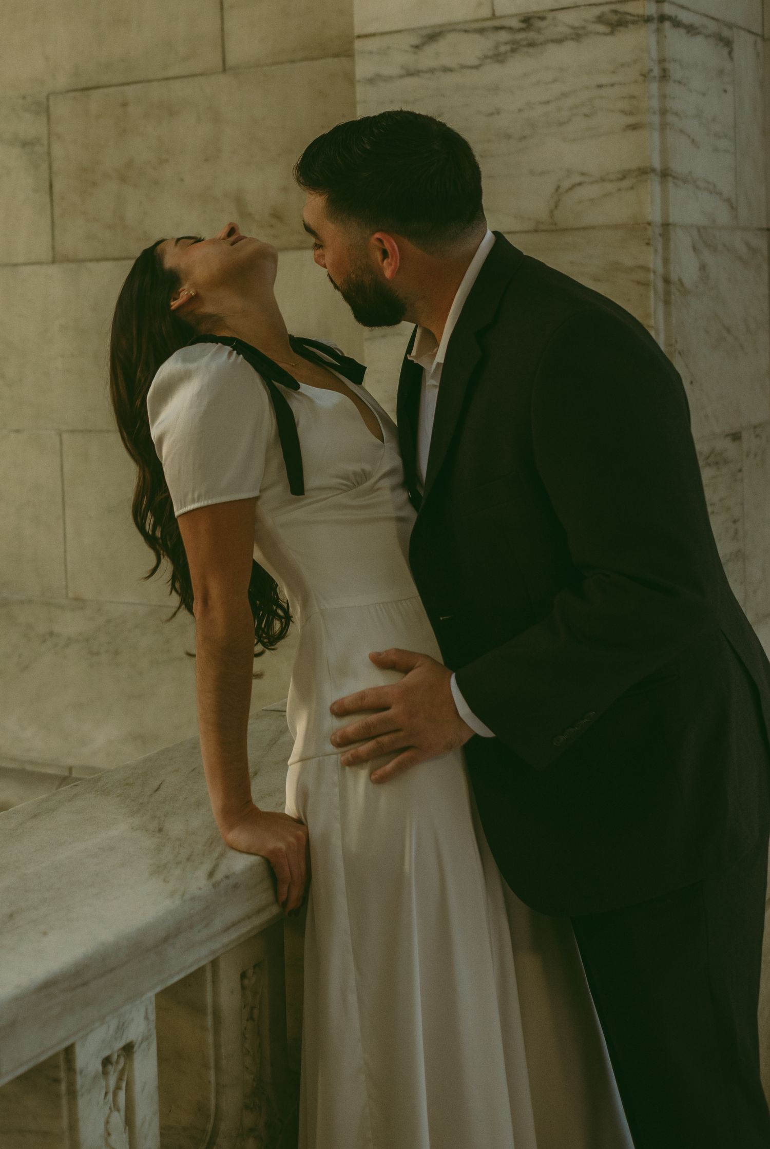 A couple shares an intimate embrace in an elegant marble hallway.