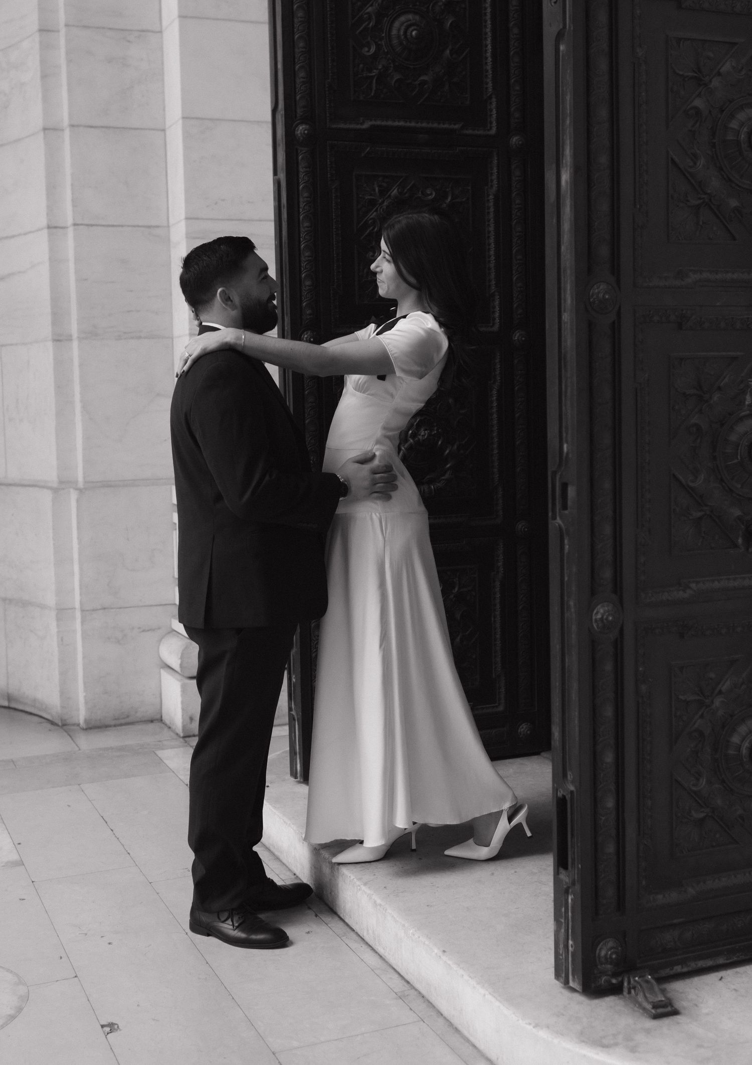 Two people in black and white formal wear standing by an ornate door.