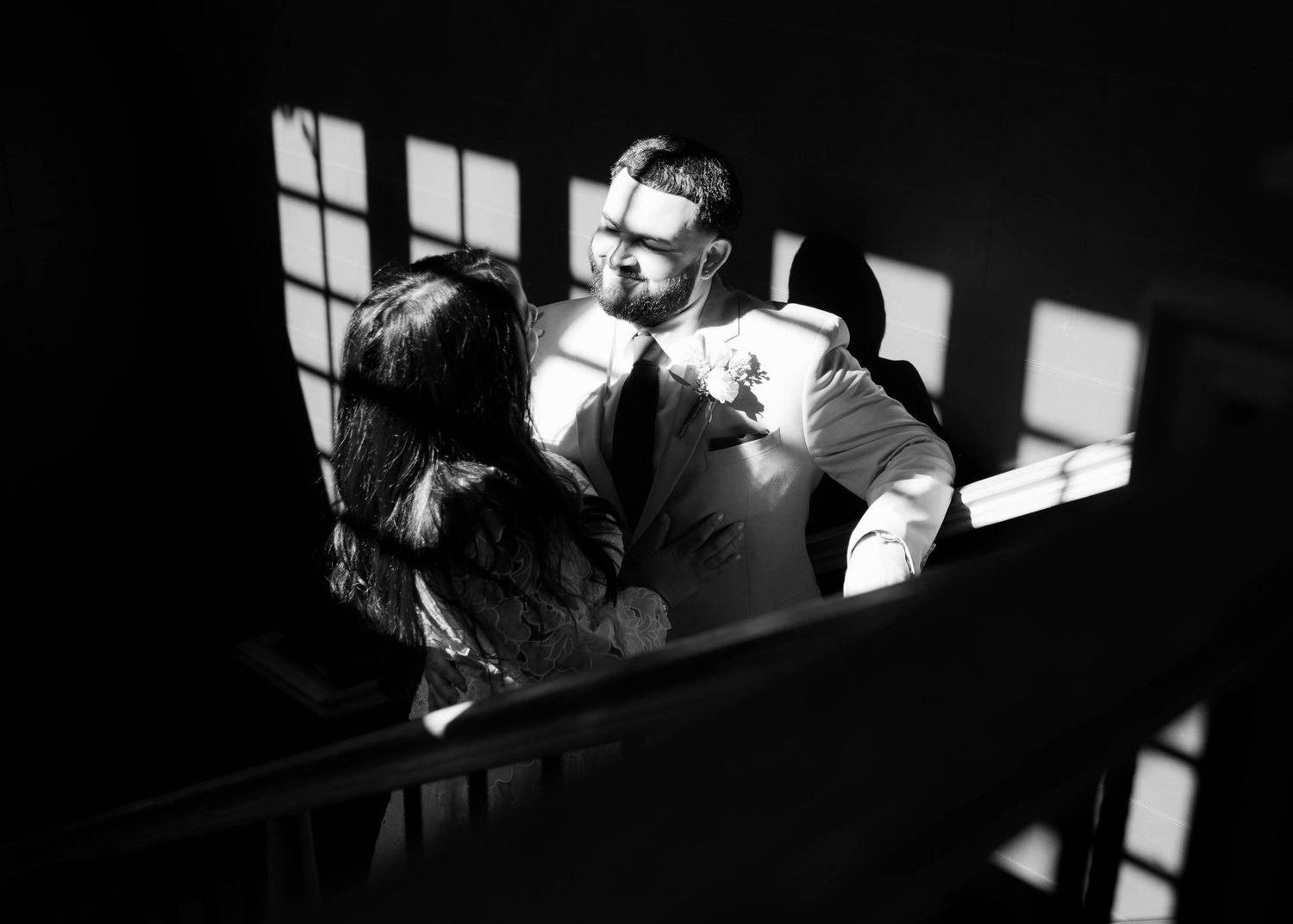 Sunlight casts geometric shadows through windows onto a dark wooden staircase.
