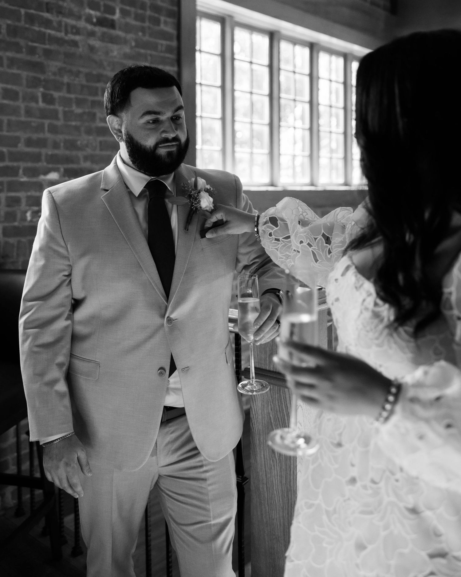 Elegant couple in formal attire shares intimate moments in brick-walled venue.