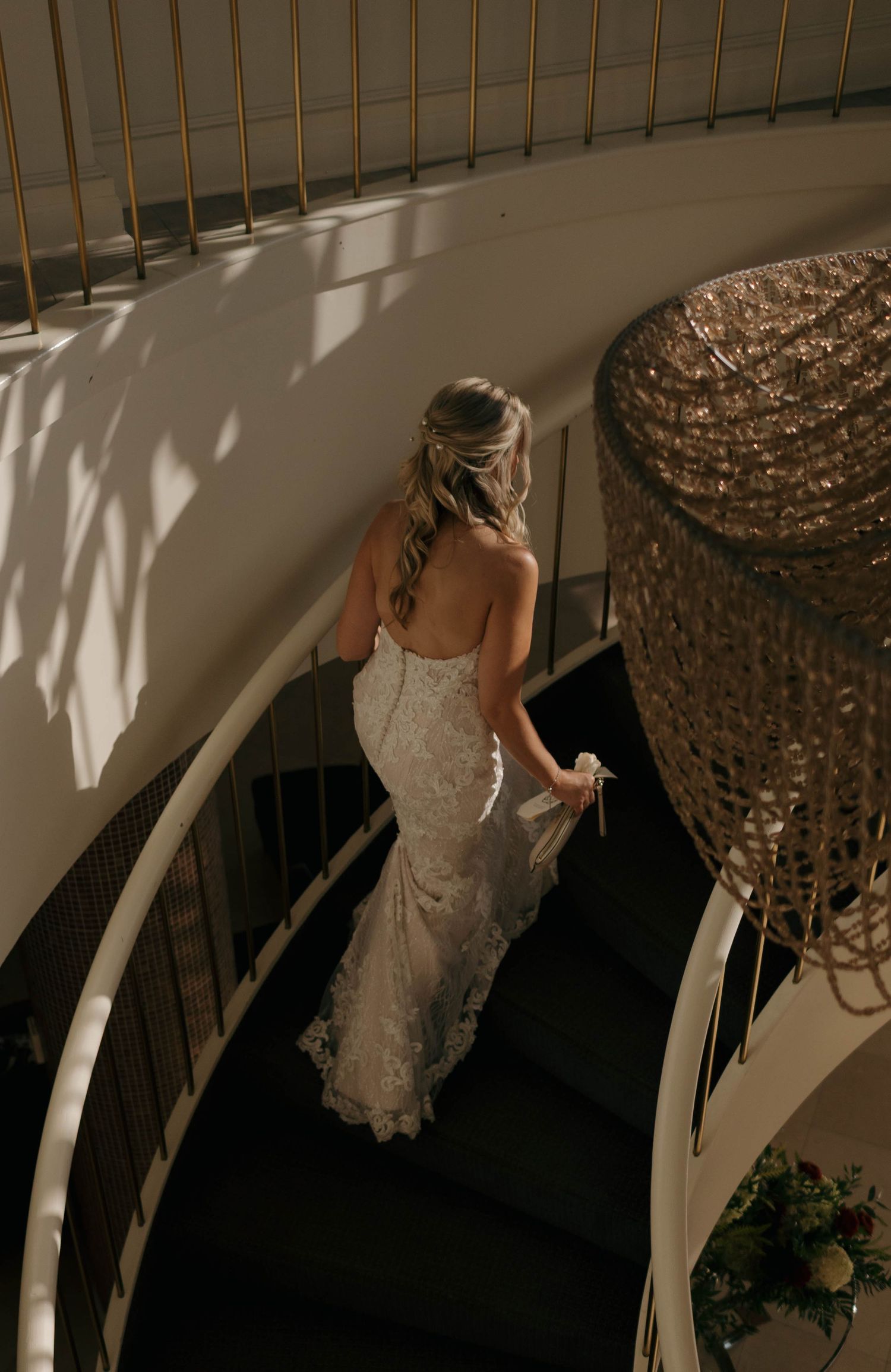 A bride in a fitted lace gown gracefully walks down a modern curved staircase.