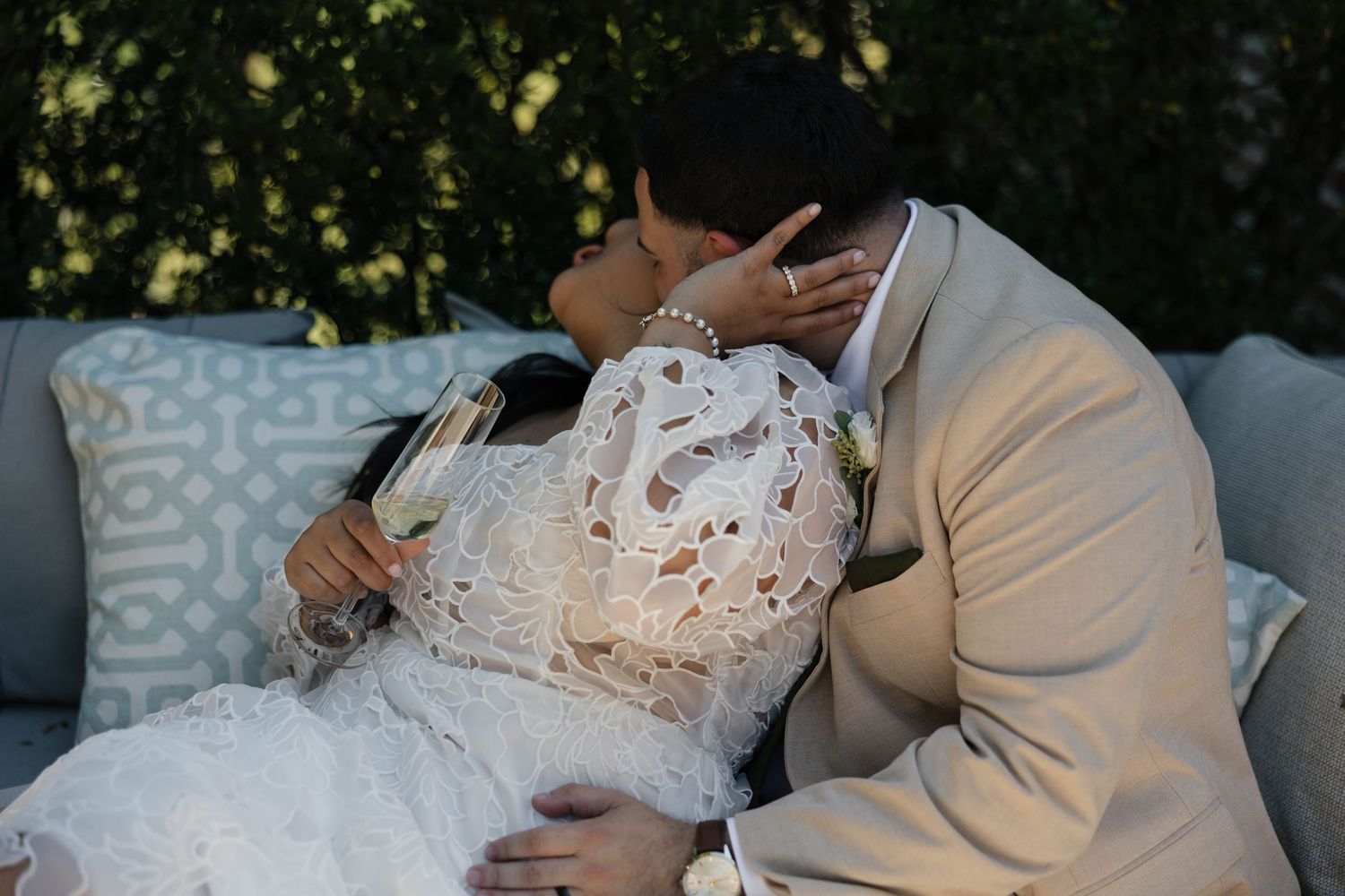 A romantic wedding moment captured on a grey couch with delicate lace details on the bride's dress.