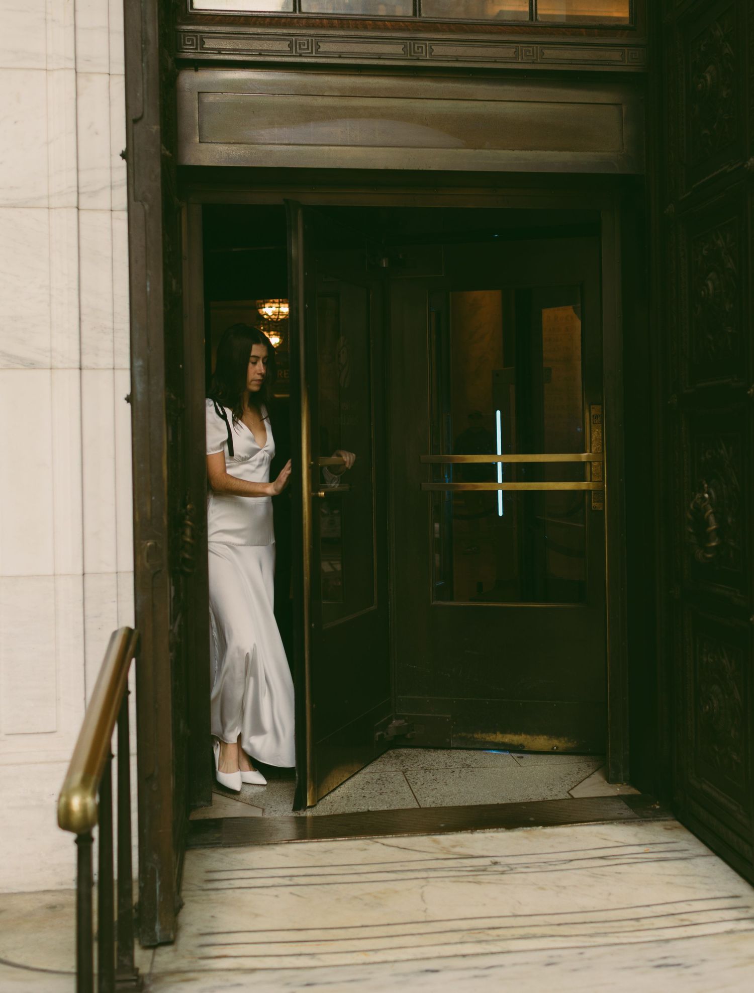 A person in a white dress stands in an elegant doorway with dramatic lighting.