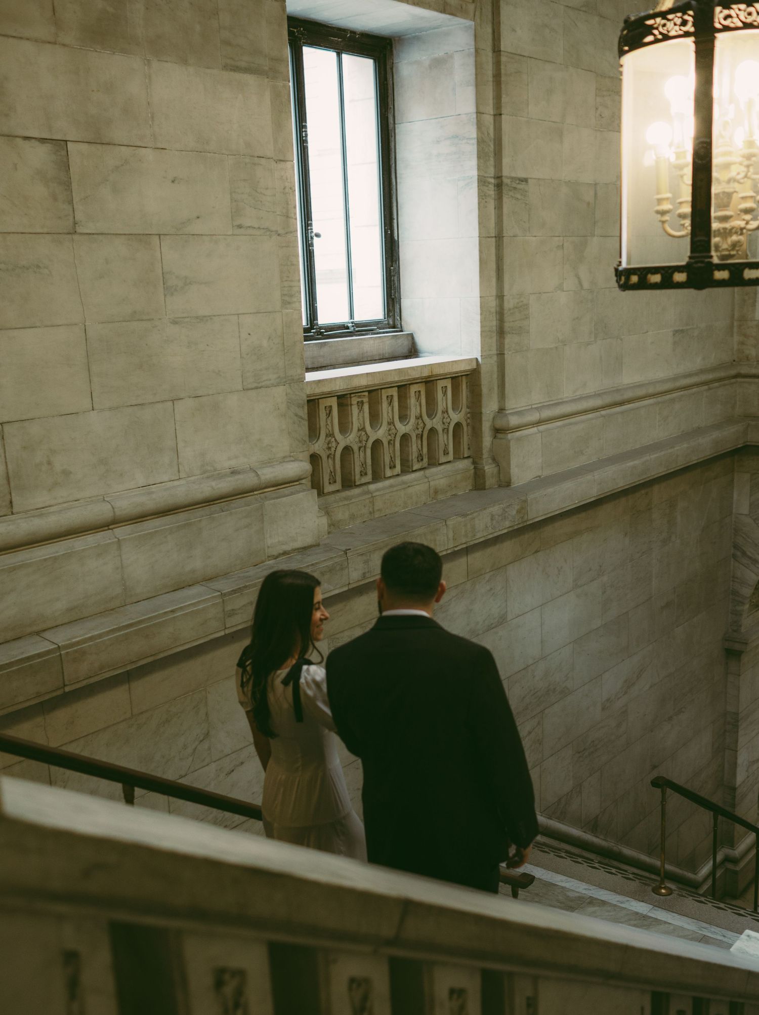 A couple walks through a historic marble building with elegant architectural details.