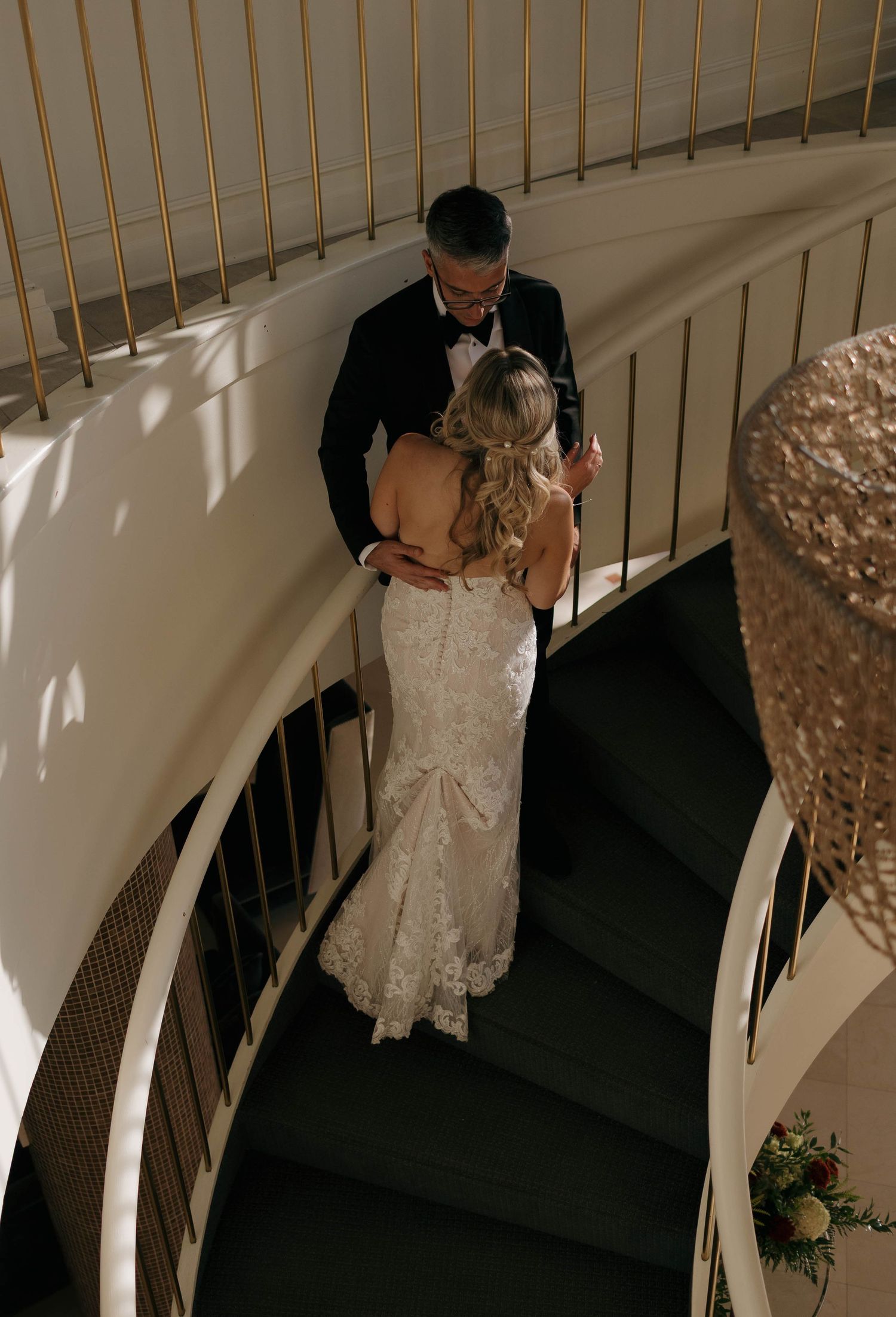 A couple shares an intimate moment on an elegant spiral staircase during their wedding day.