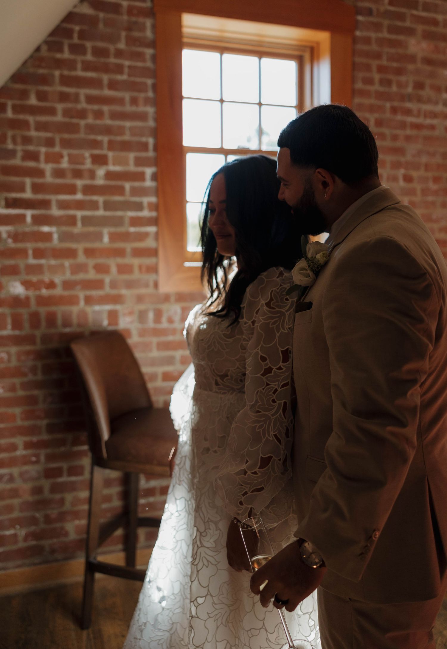 Wedding couple shares tender moment in rustic brick venue with warm lighting.