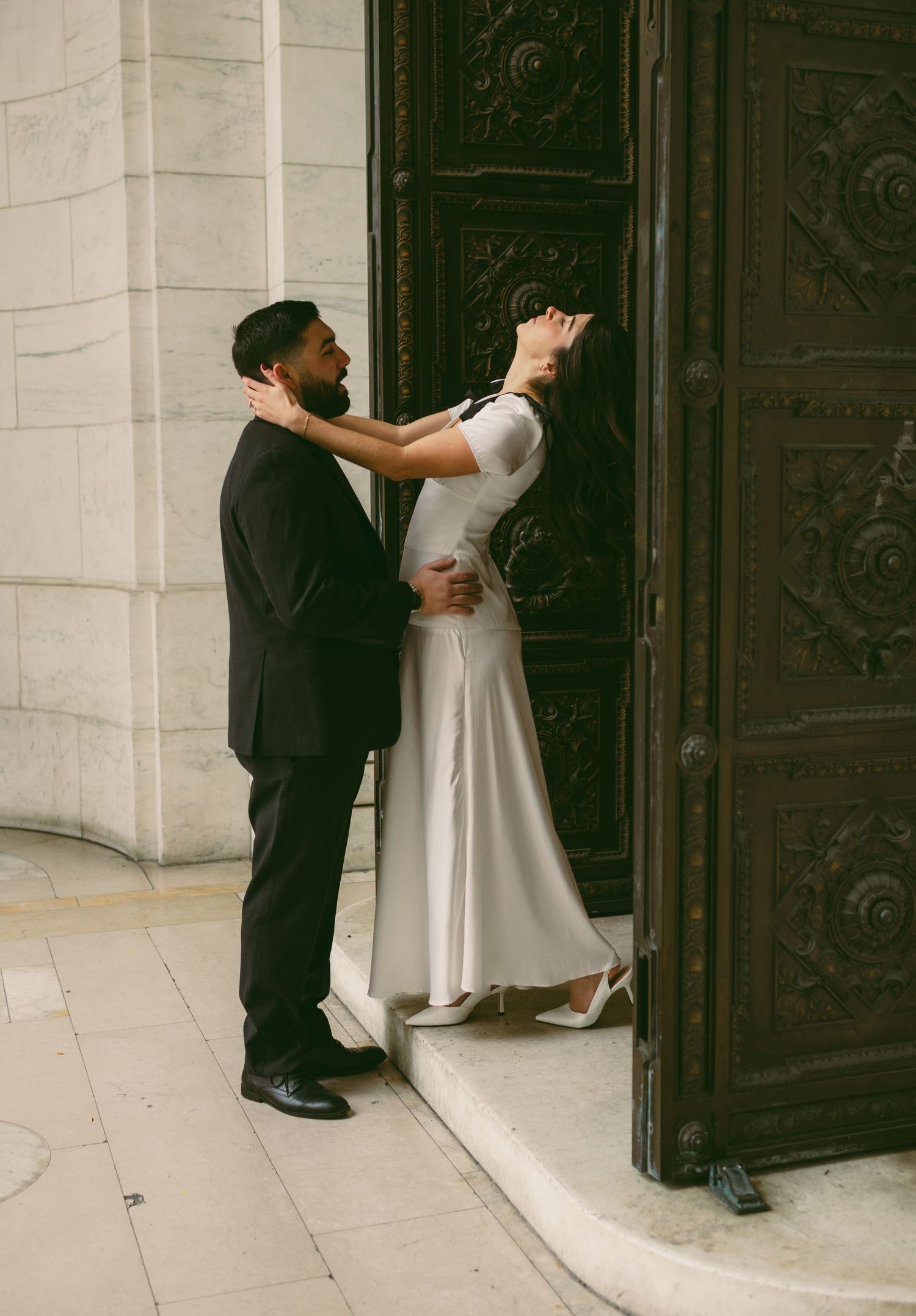 A couple in formal attire interacting near an elegant building entrance.