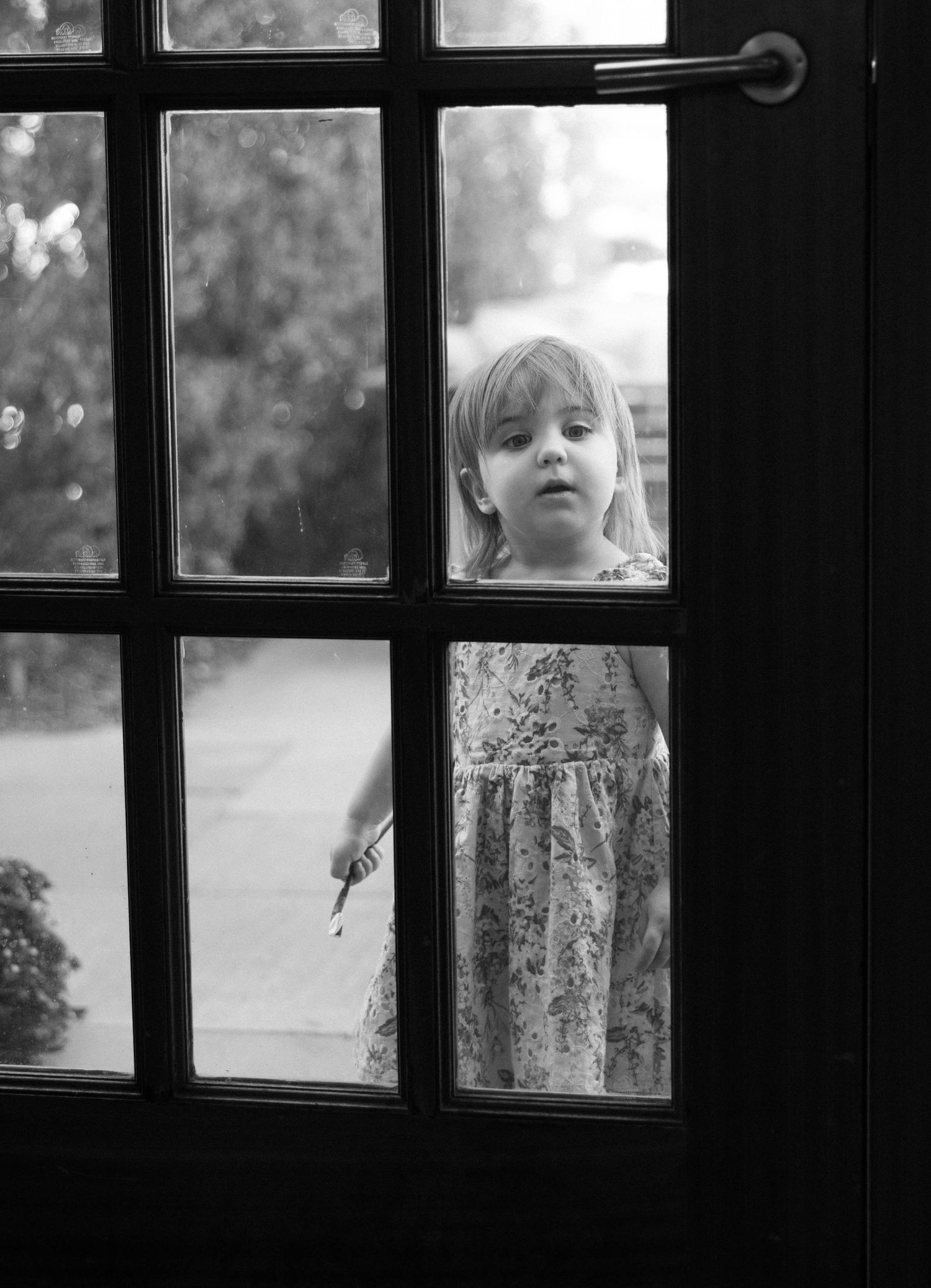 A black and white photo of a child peering through windowpanes with a curious expression.