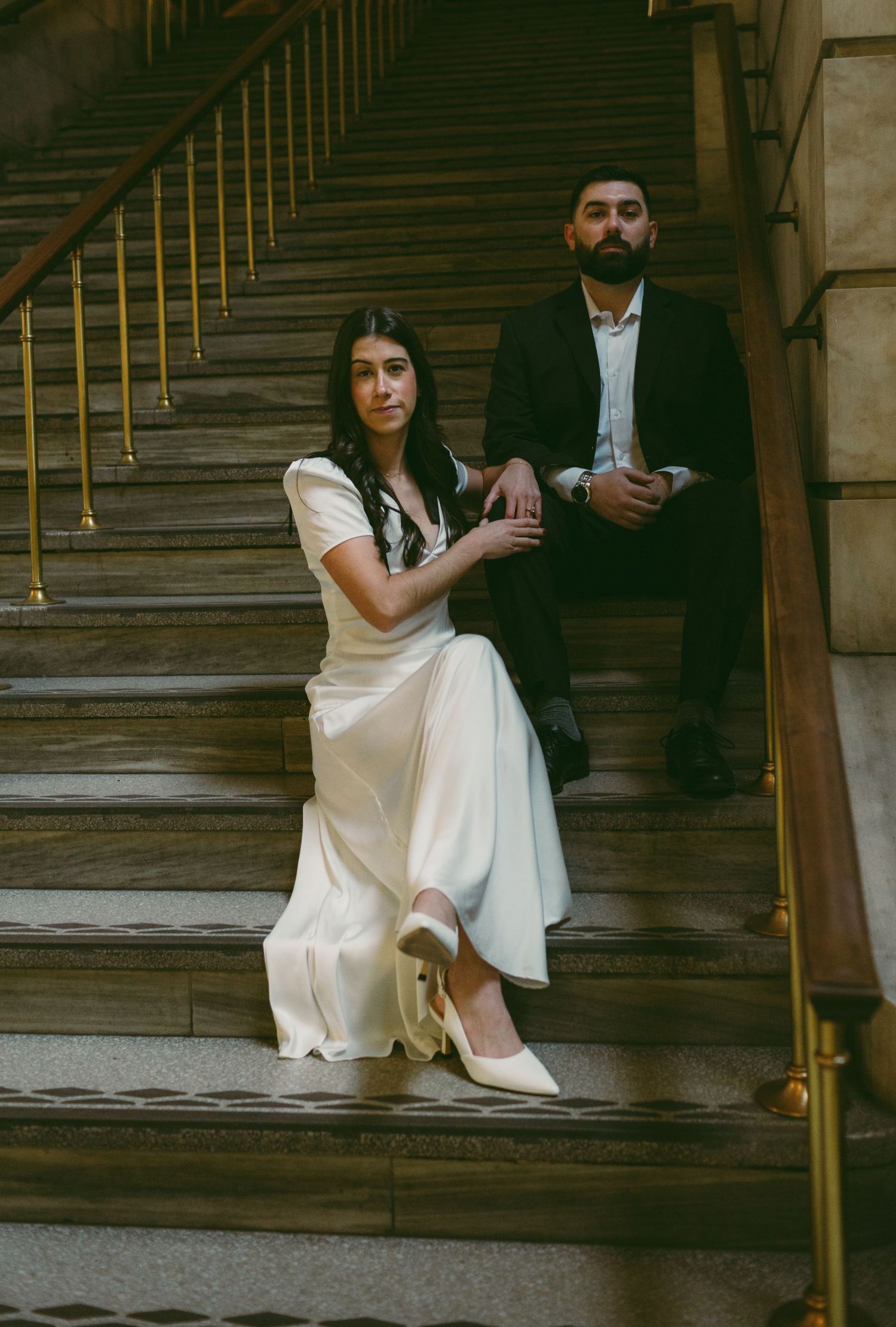Couple sitting on grand stone steps in formal wear.