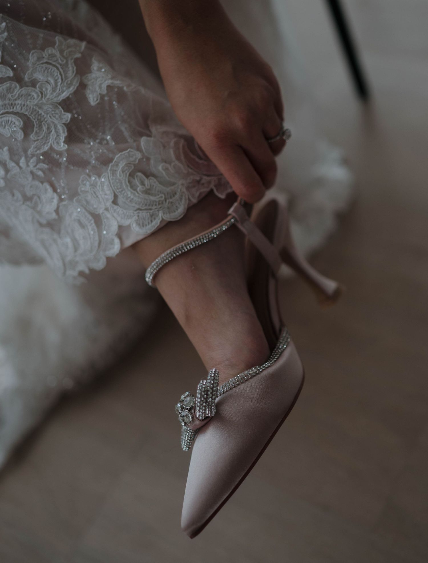 Close-up of an elegant bridal shoe being fastened with delicate lace details.