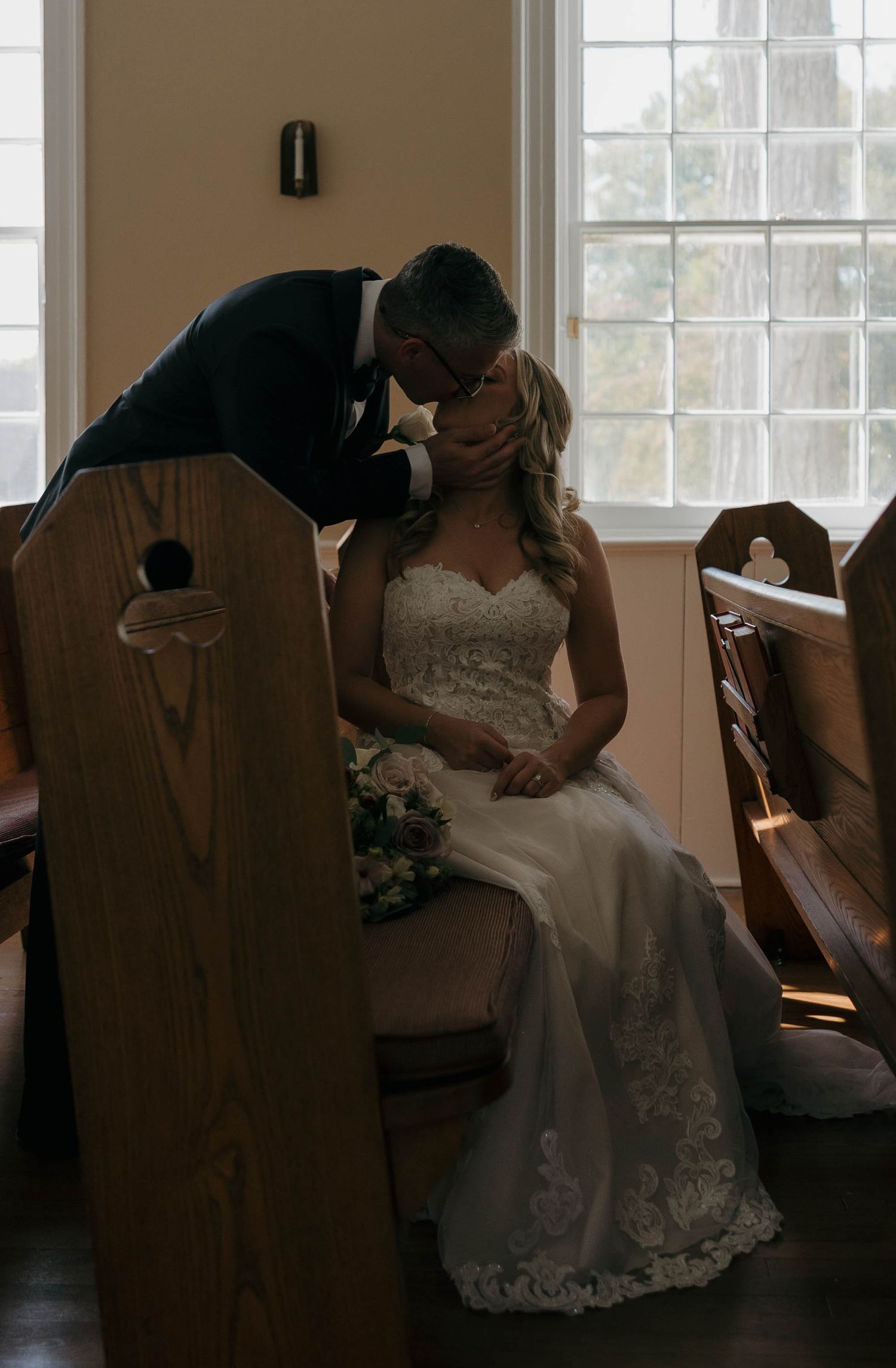 A romantic wedding scene with sunlight streaming through windows behind wooden church pews.
