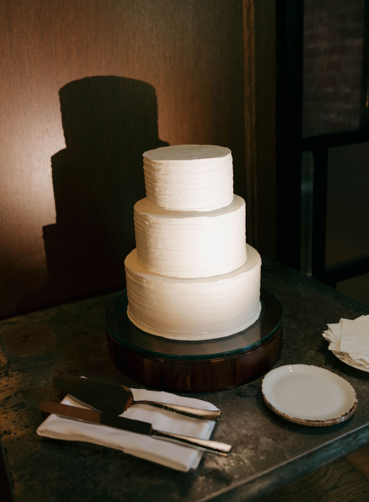 Simple three-tiered white wedding cake displayed on rustic wooden stand.