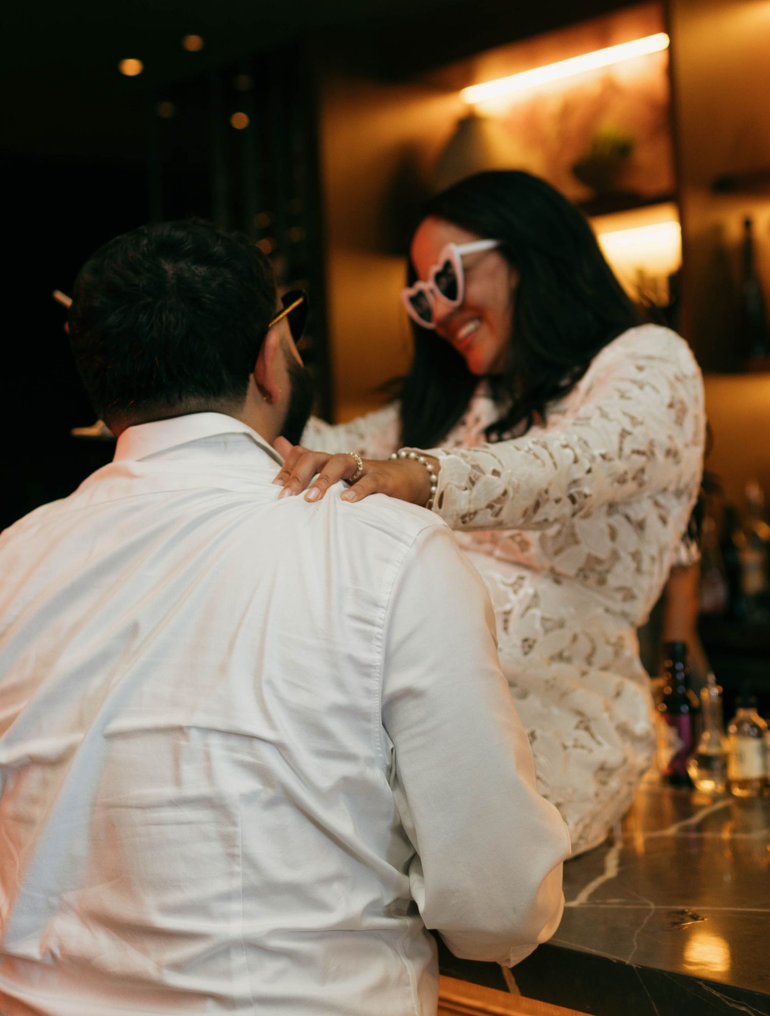 A couple dancing together at a dimly lit bar, with one person wearing white and the other in a patterned dress.