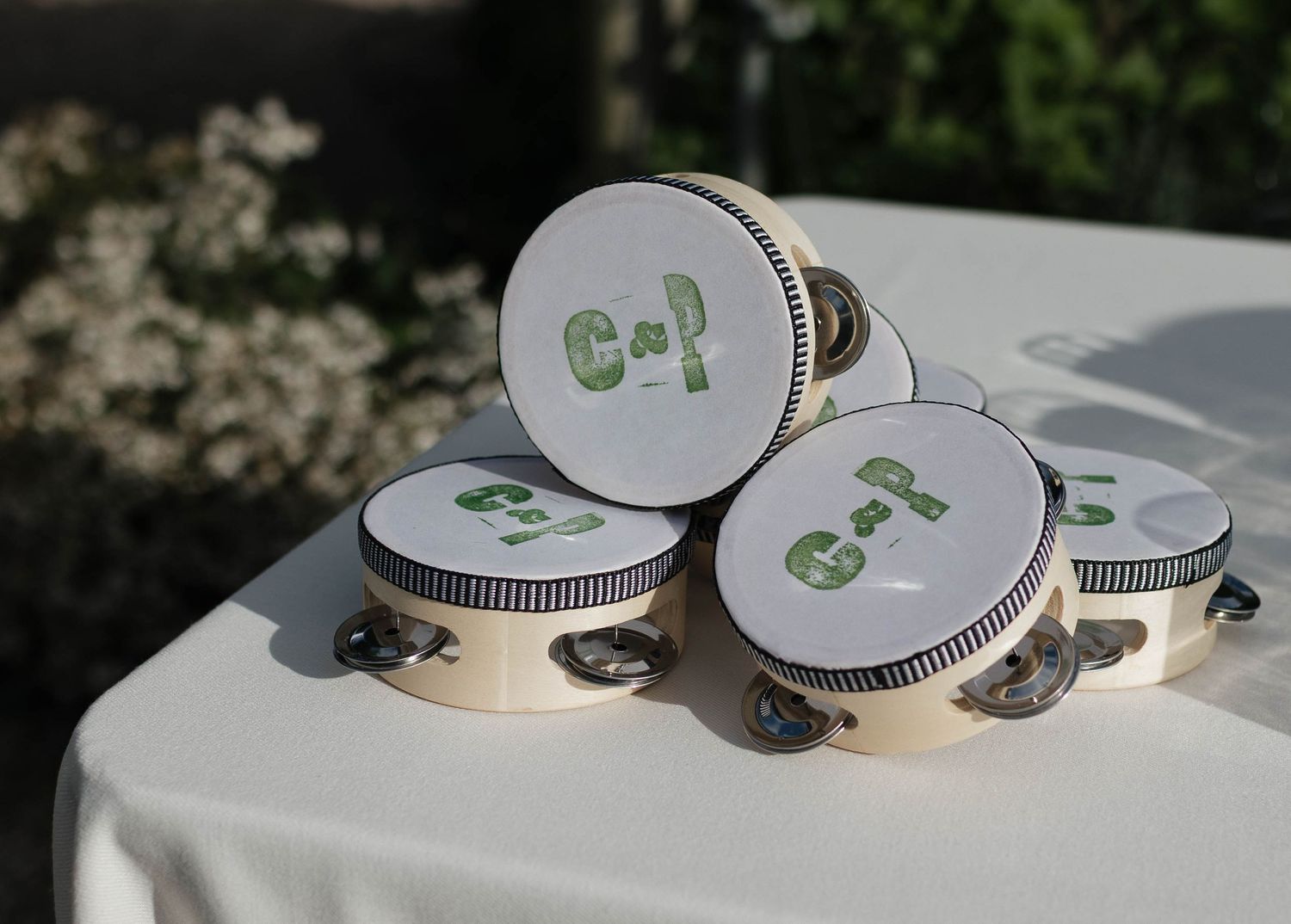 White tambourines with green monogram letters arranged on an outdoor table in sunlight.