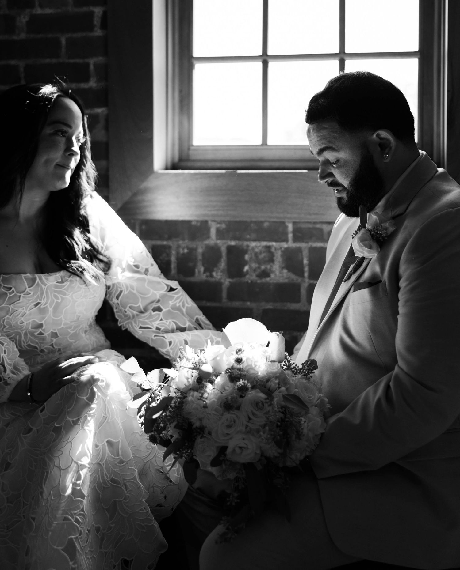 Silhouetted figures share tender moments near a bright window in a brick-walled room.