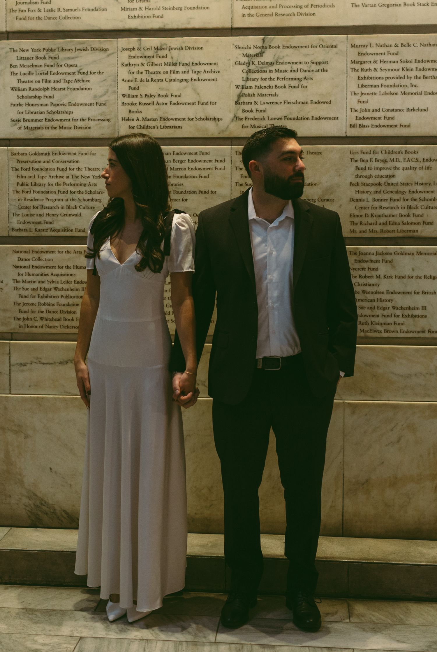 Couple in formal wear standing against wall with text displays.