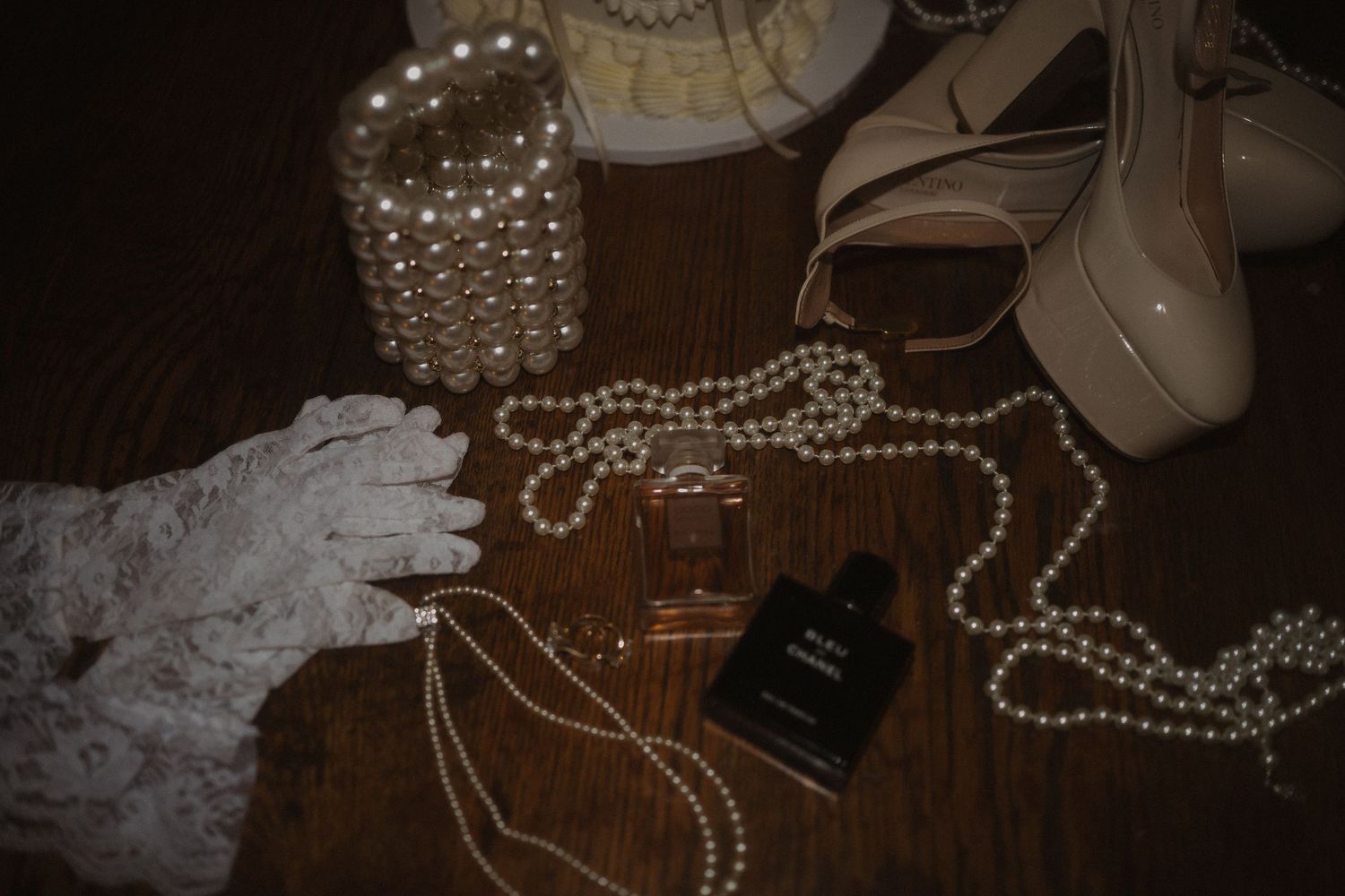 Wedding accessories including pearl necklaces, shoes, and lace arranged on dark wooden surface.