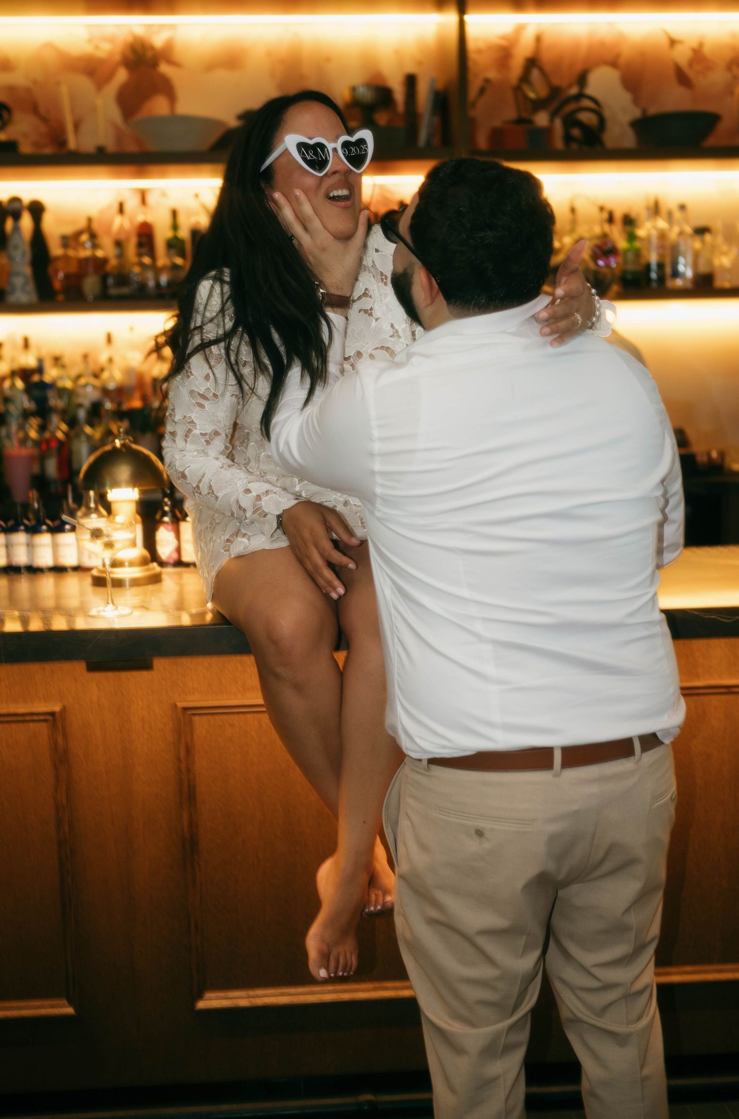 Couple dancing intimately at a bar with warm golden lighting and bottles displayed in background.