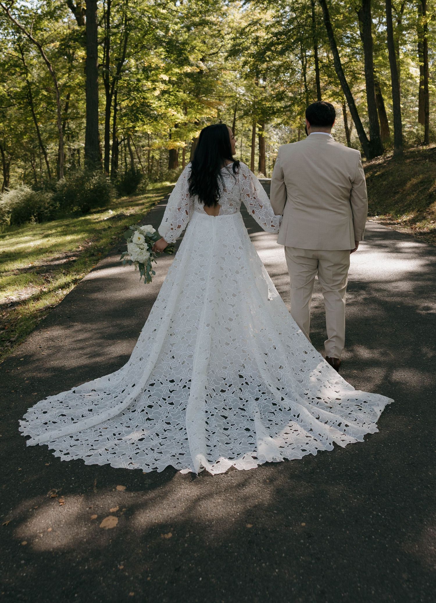 Wedding couple walking on forest path with bride's lace train trailing behind.
