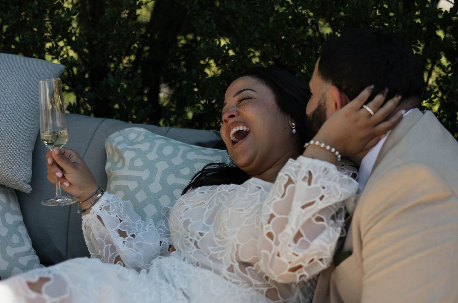 Candid moment of couple sharing laughter while relaxing at outdoor wedding reception.