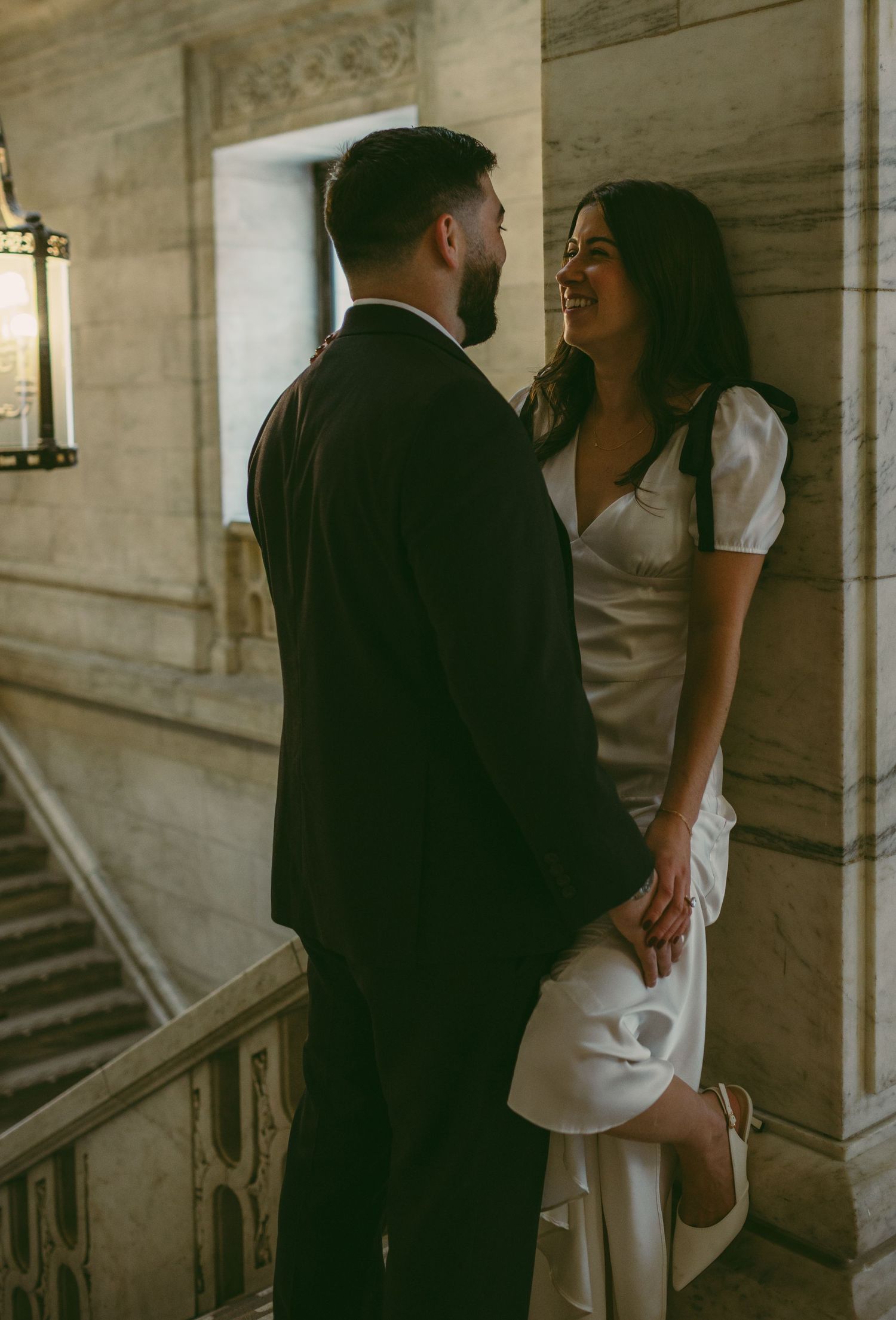 A romantic moment between a couple in formal attire standing in a grand marble hallway.