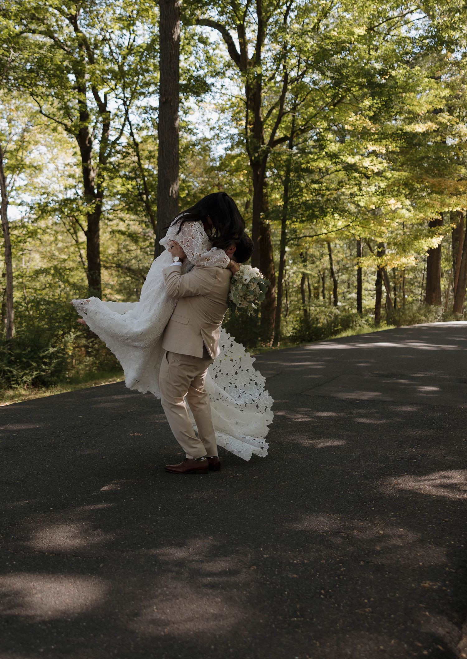 A couple performs a dramatic dance lift on a forest path surrounded by trees.
