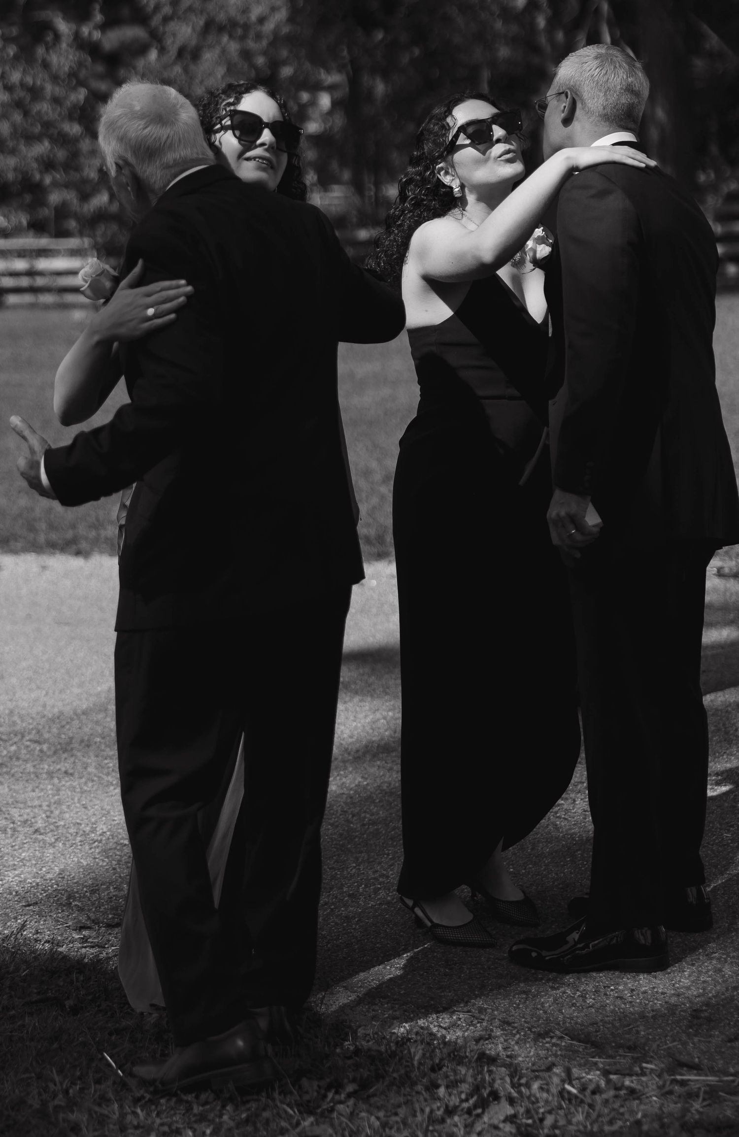 A black and white photo of formal-dressed guests embracing at an outdoor event.