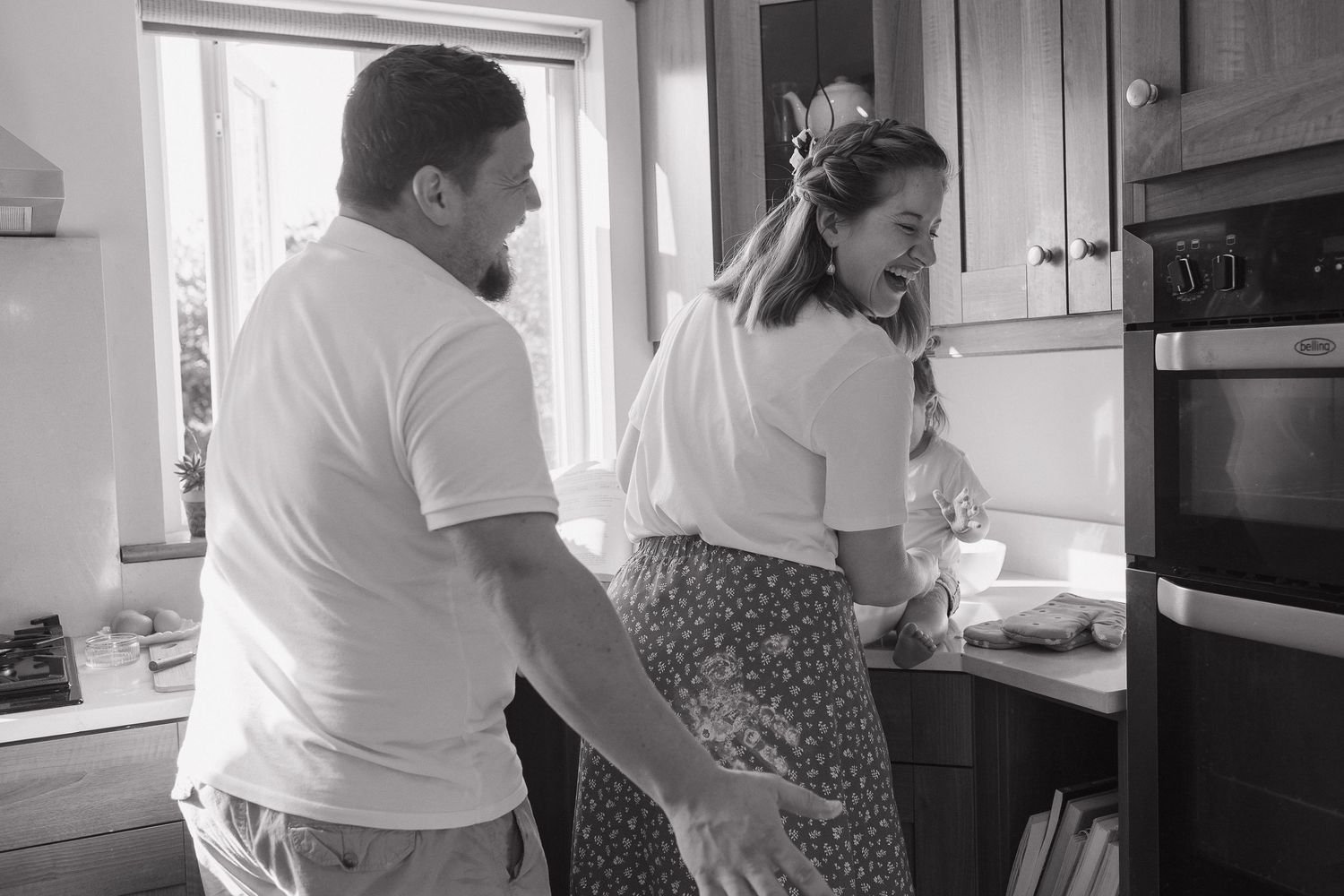 Two people prepare food together in a bright white kitchen with sunlight streaming through the windows.